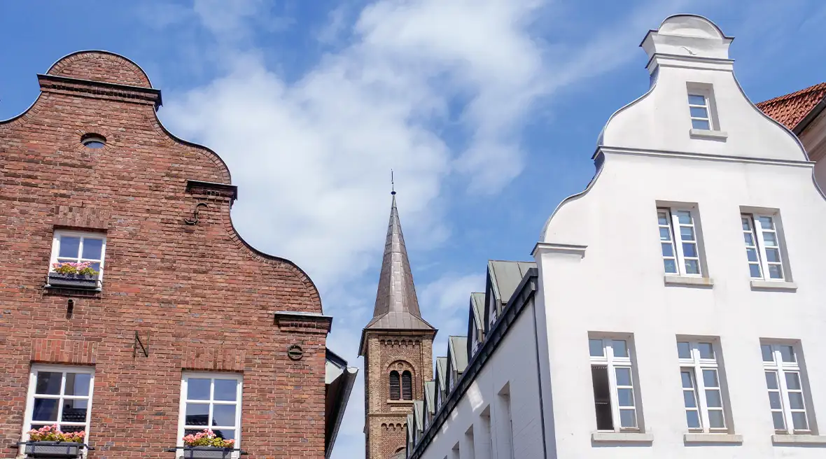 Two gables of old houses with a church spire between them