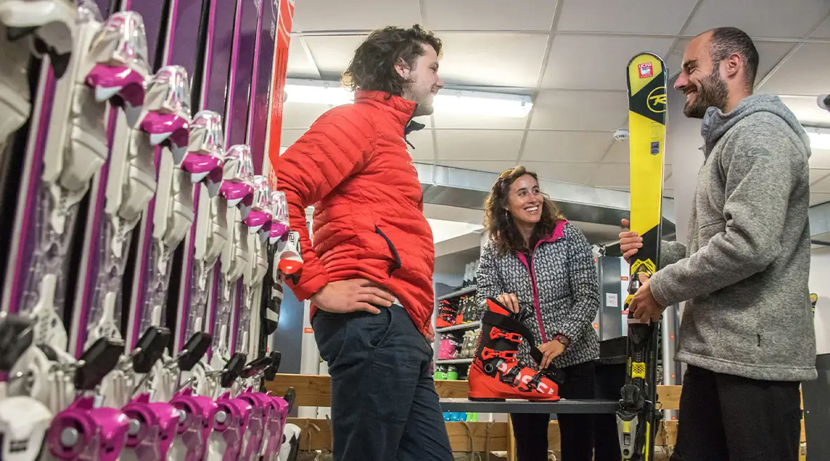 Two men and a woman in the ski boot fitting room. A row of red skis in the foregrounds