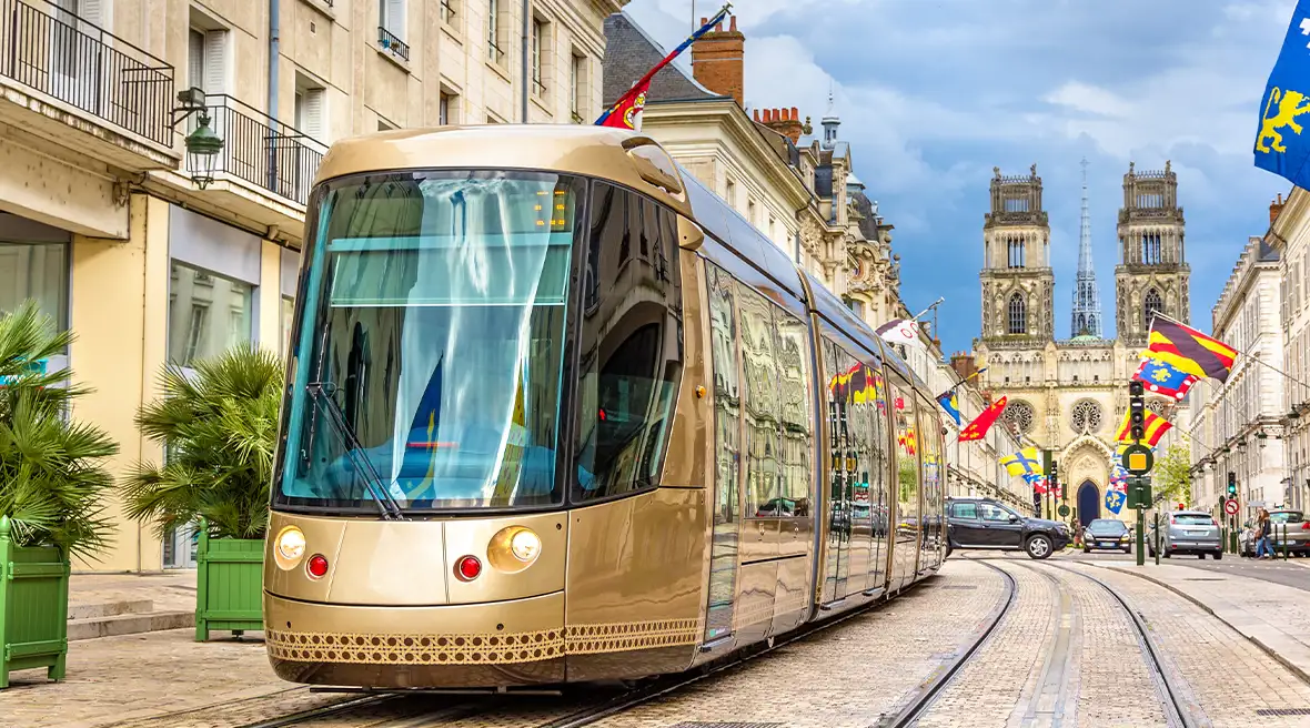 Modern gold tram travelling down a tramline in a central city street with a cathedral in the background and ceremonial flags flying from buildings