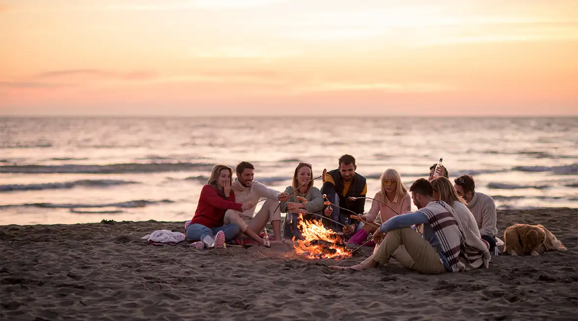 Group of friends sitting around a campfire on the beach at sunset