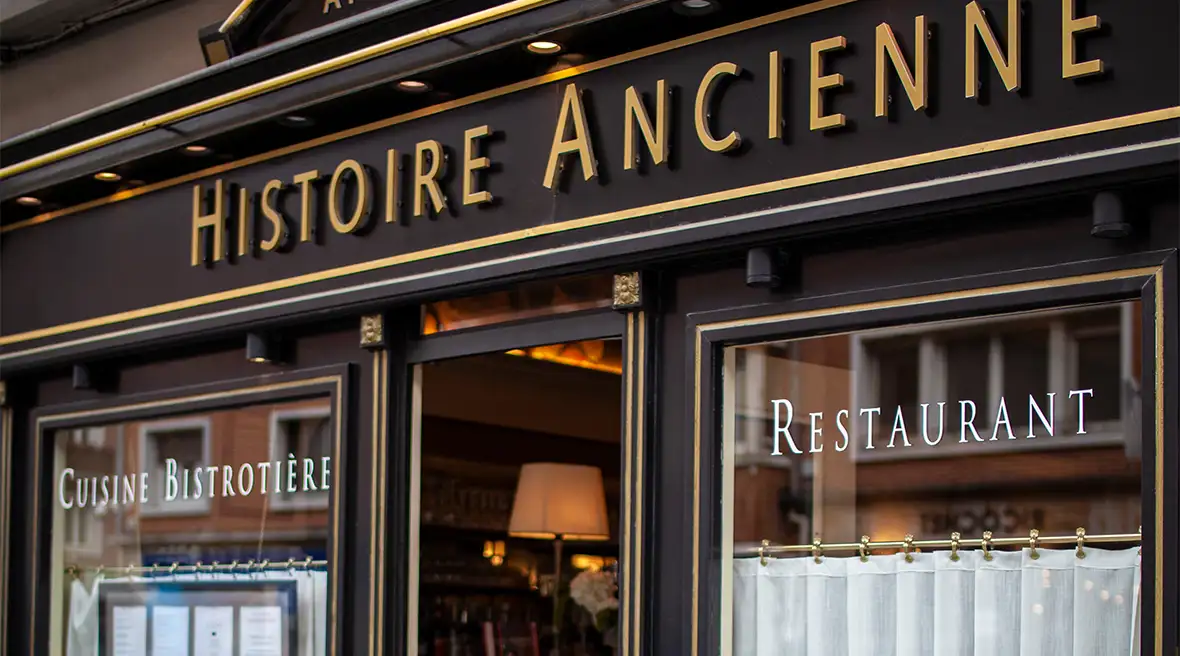 The front of a brasserie restaurant with a door in the middle of two big windows, dark brown surround and the words Histoire Ancienne above the door in gold block capitals