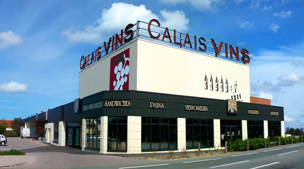An exterior view of the Calais Vins shop and its large logo on the roof of the building which sits on a big corner plot in an industrial estate and adjoins a boulangerie and patisserie.