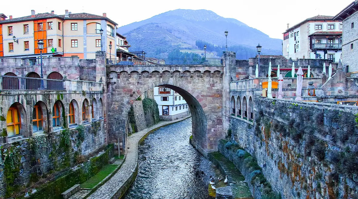 Cantabria is filled with traditional towns like Potes -tag: river running through an old Spanish town with mountains in the distance