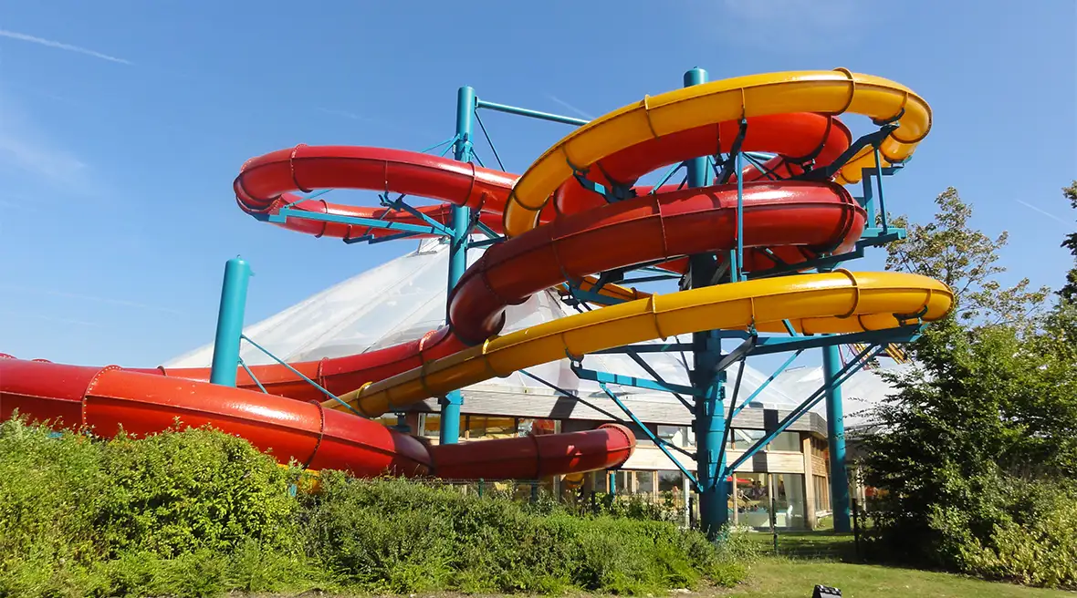 Red and yellow water slides snake around each other outside a water park on a summer’s day