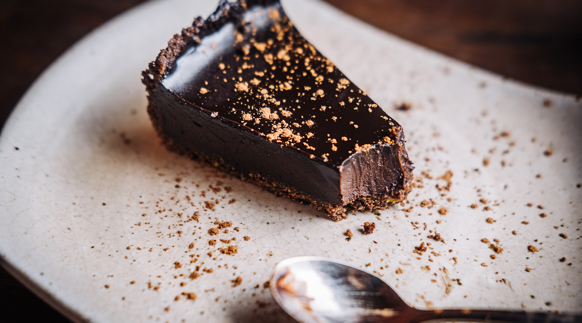 Slice of half-eaten dark chocolate cake on a white plate with a spoon