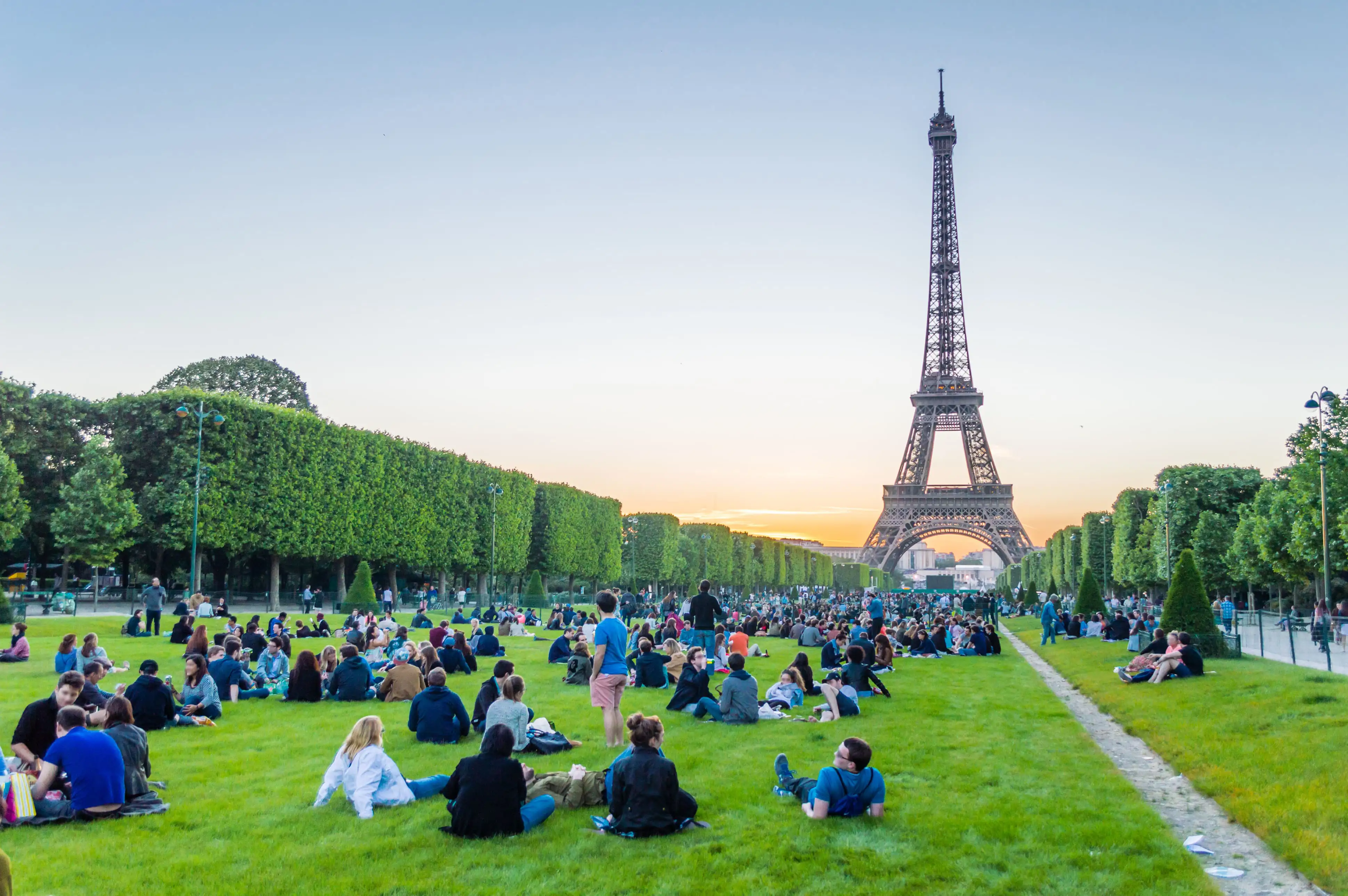 People relaxing on the grass at Parc du Champ de Mars with the Eiffel Tower in the background.