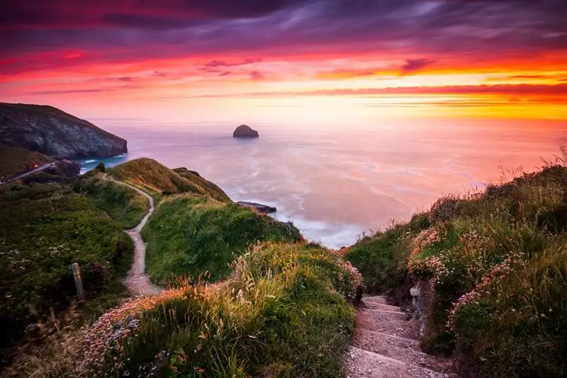 Parmi les rochers herbeux, un escalier menant à la plage et ciel de crépuscule jaune-rouge.