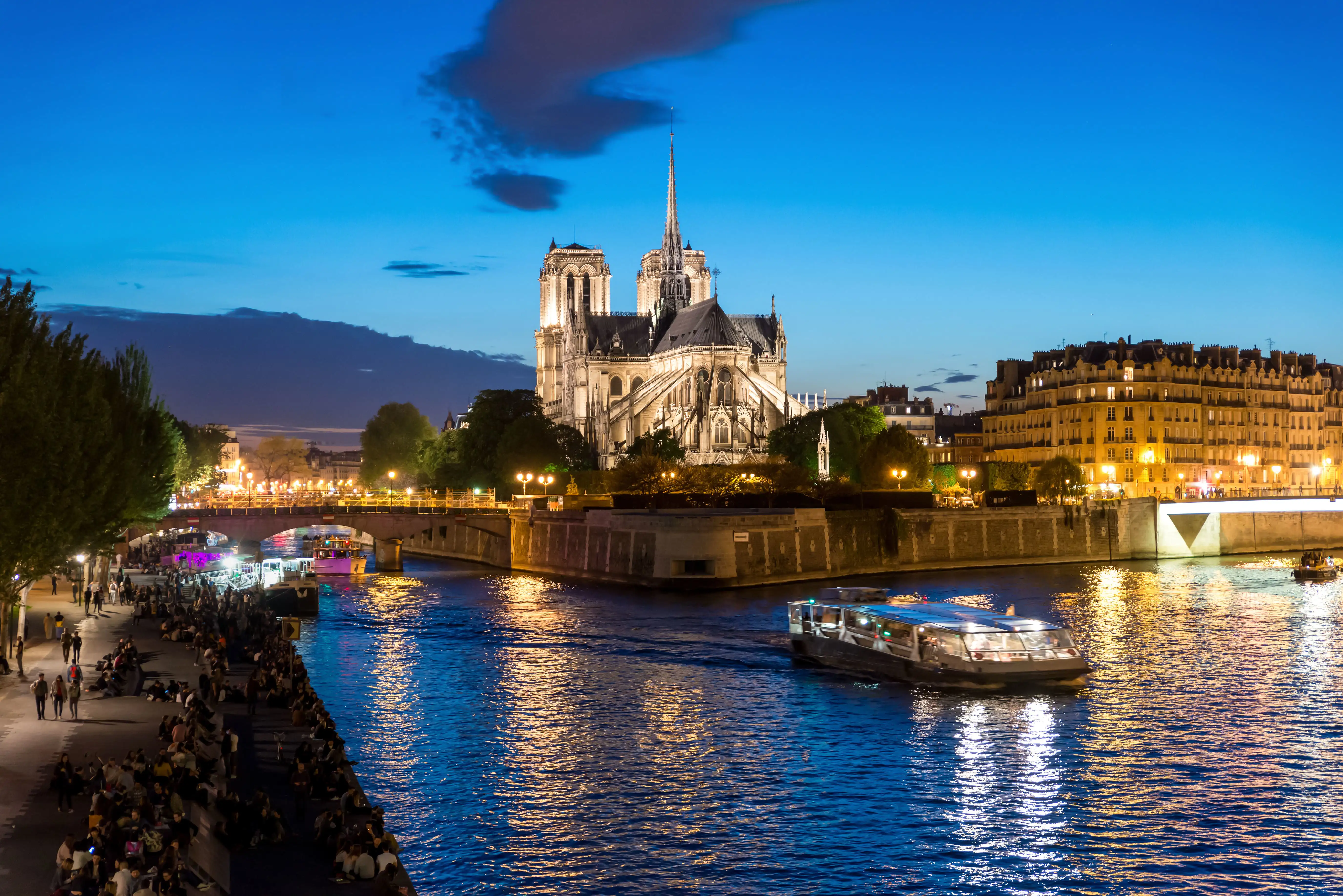 A river boat on the Seine at dusk with Notre Dame cathedral behind it