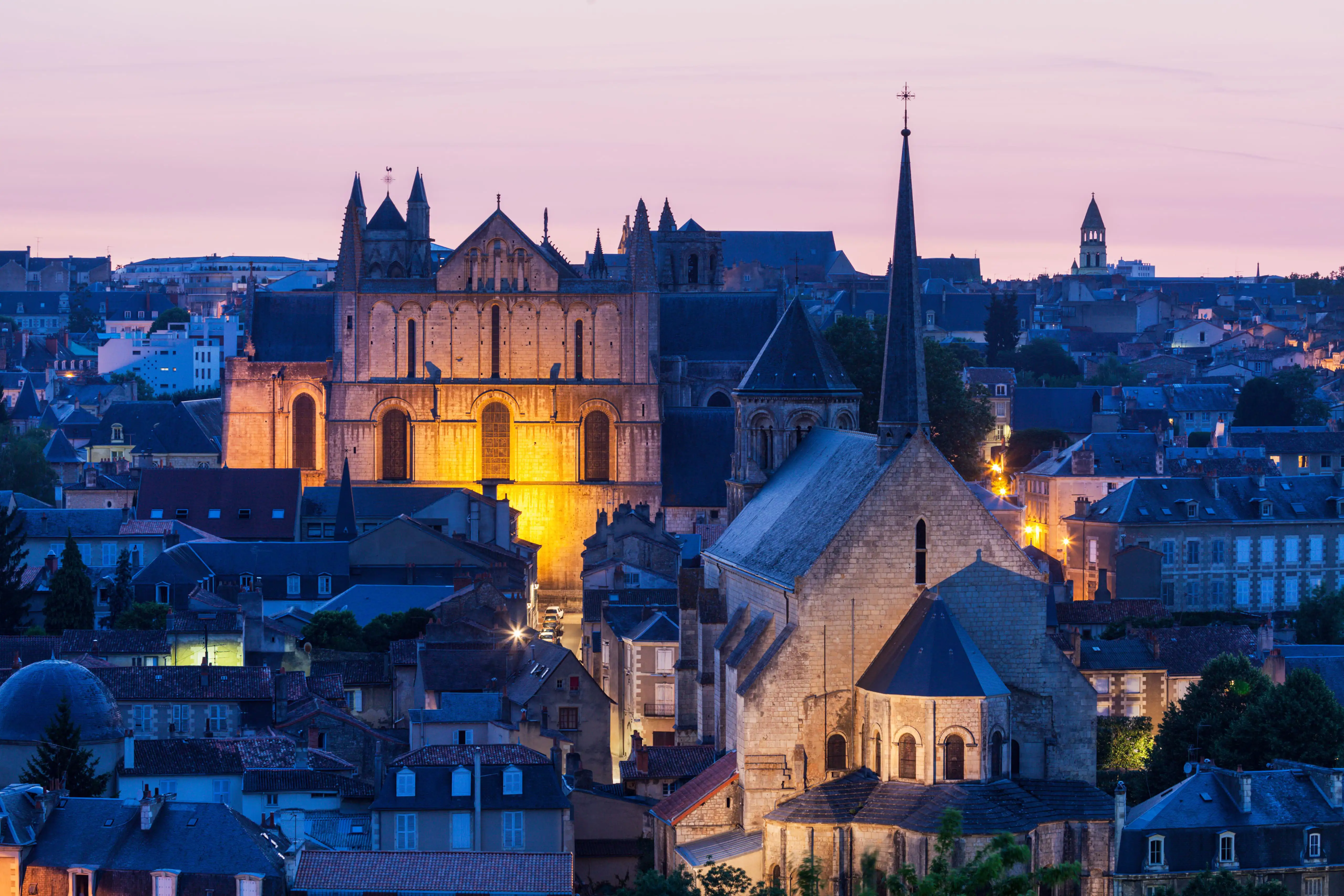 Panoramic view of Poitiers at dusk with the Cathedral of Saint Peter illuminated against a pink sky.