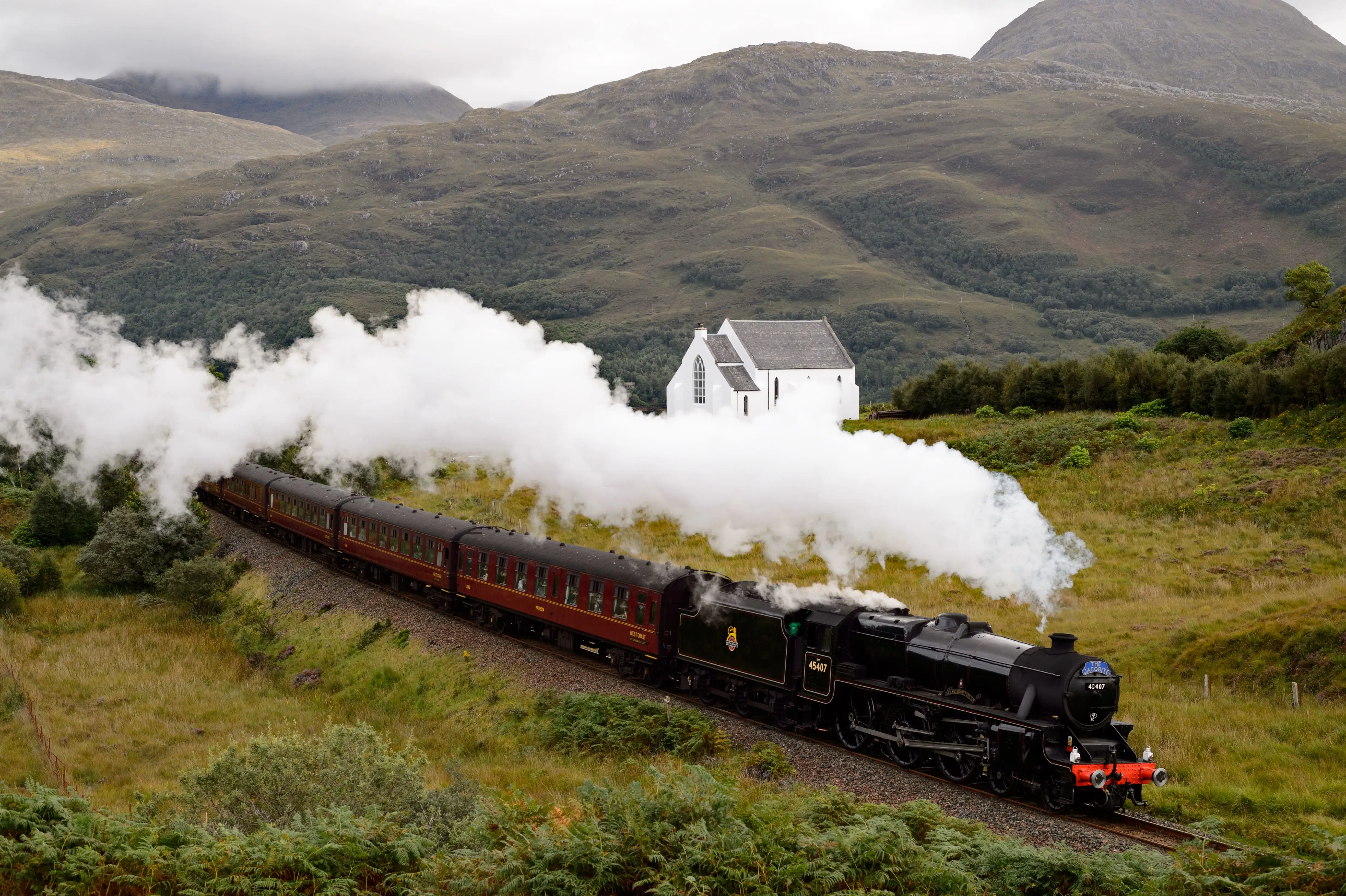 Een rijdende stoomtrein in een bergachtig landschap.