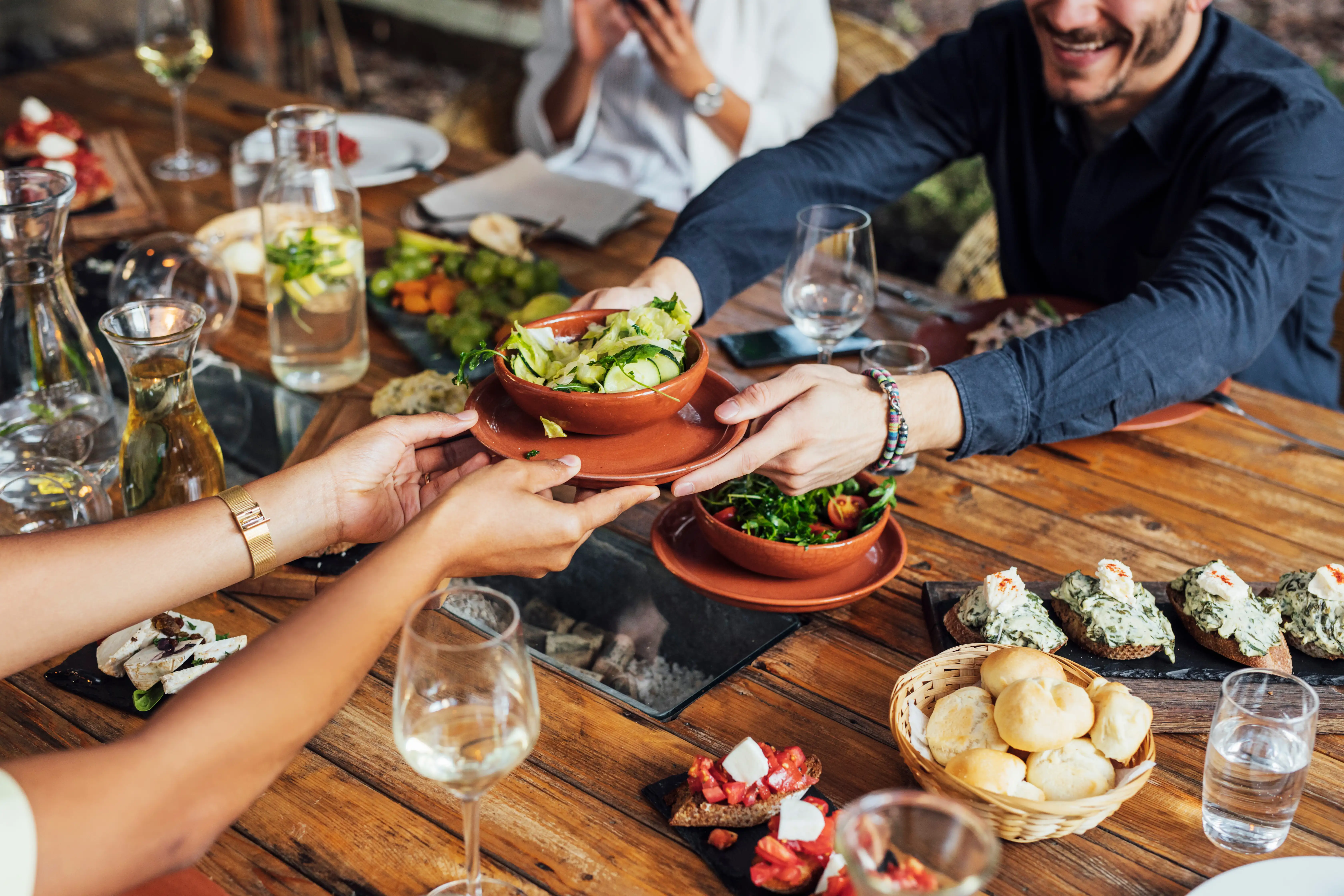 A man passing a bowl of salad to another diner at a table