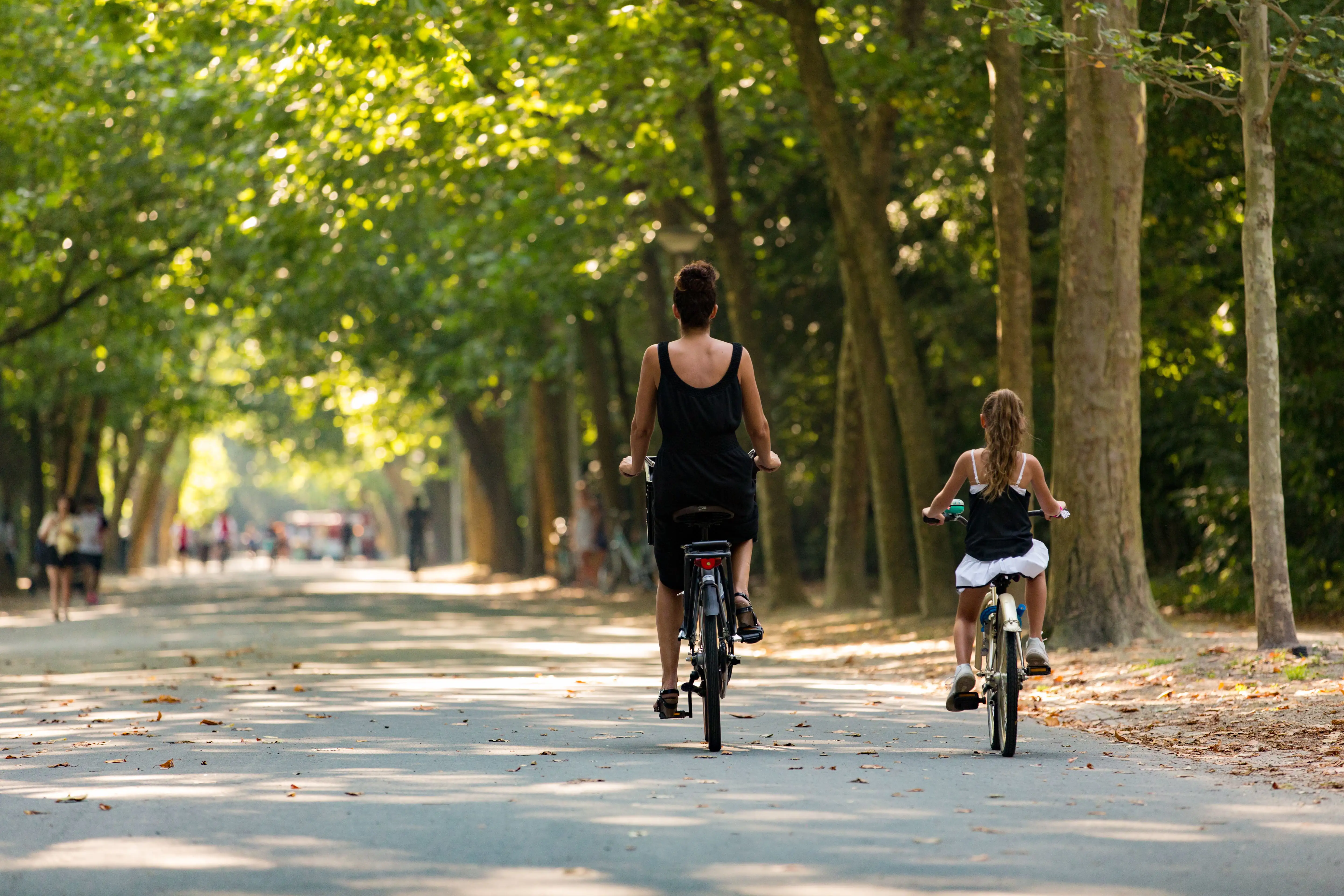 A mother and child cycling along a broad path, in Vondelpark, Amsterdam