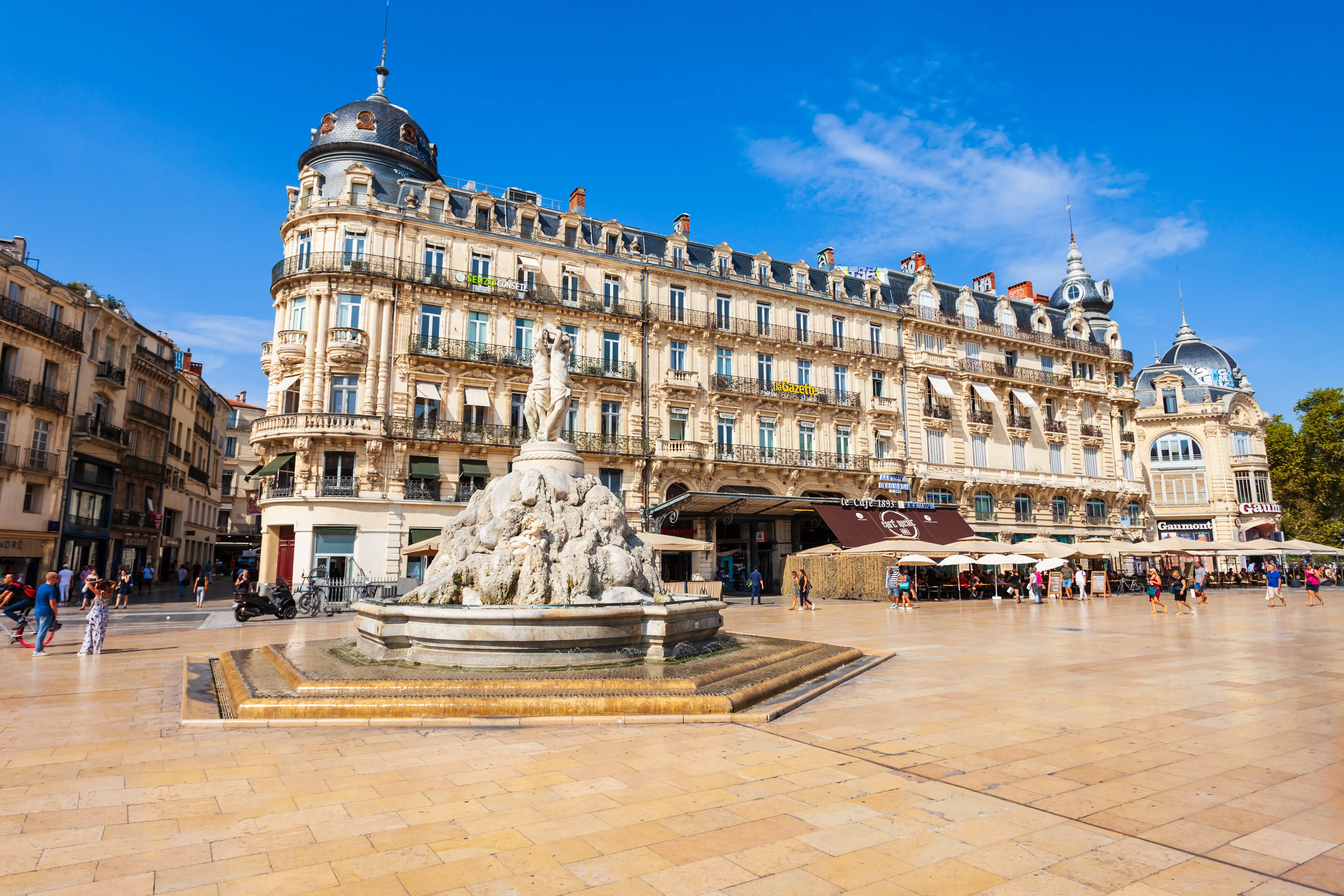 A decorative stone fountain in front of a large Parisian style building in a large city square