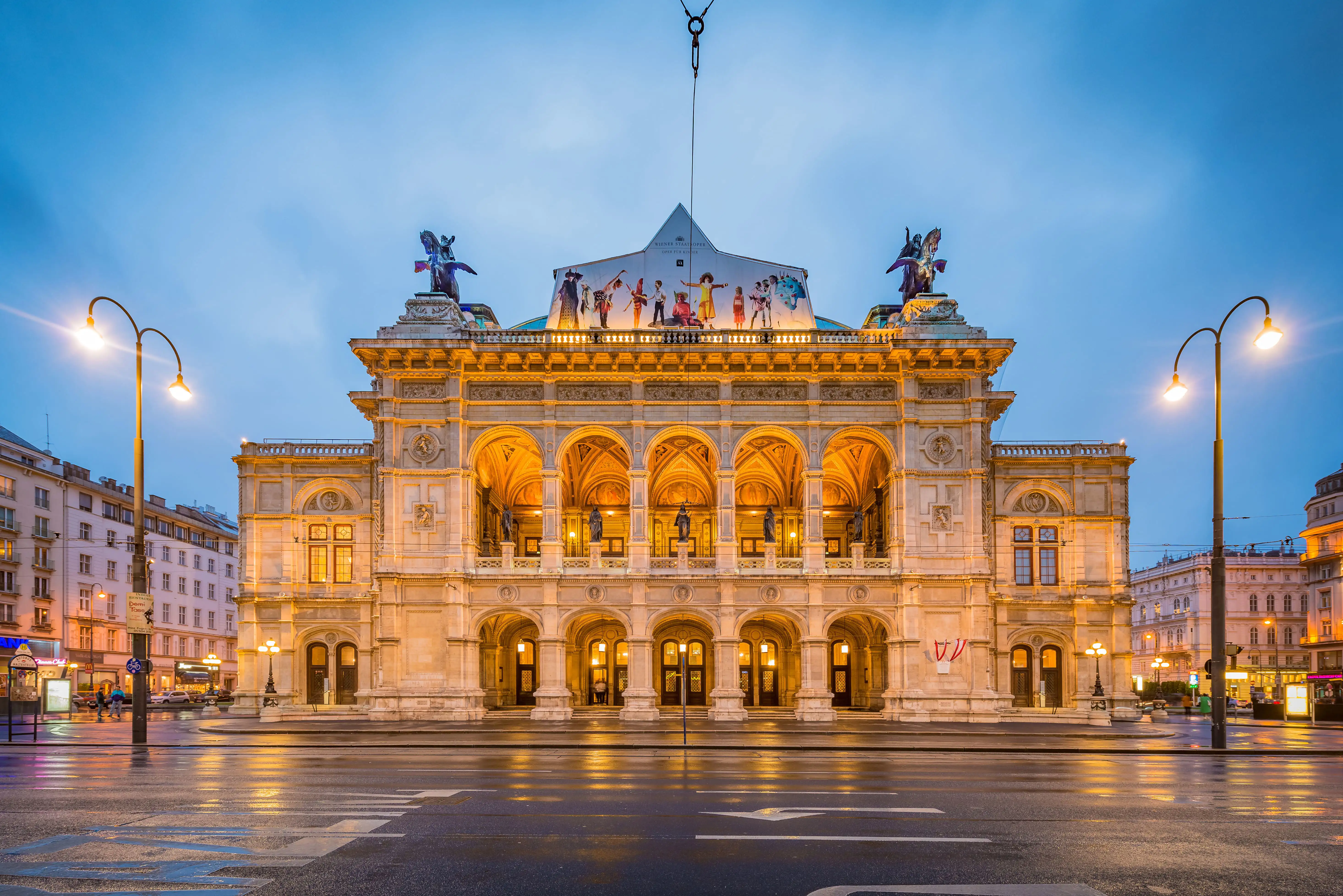 Vienna State Opera illuminated in warm evening lights, showcasing its grand architecture.