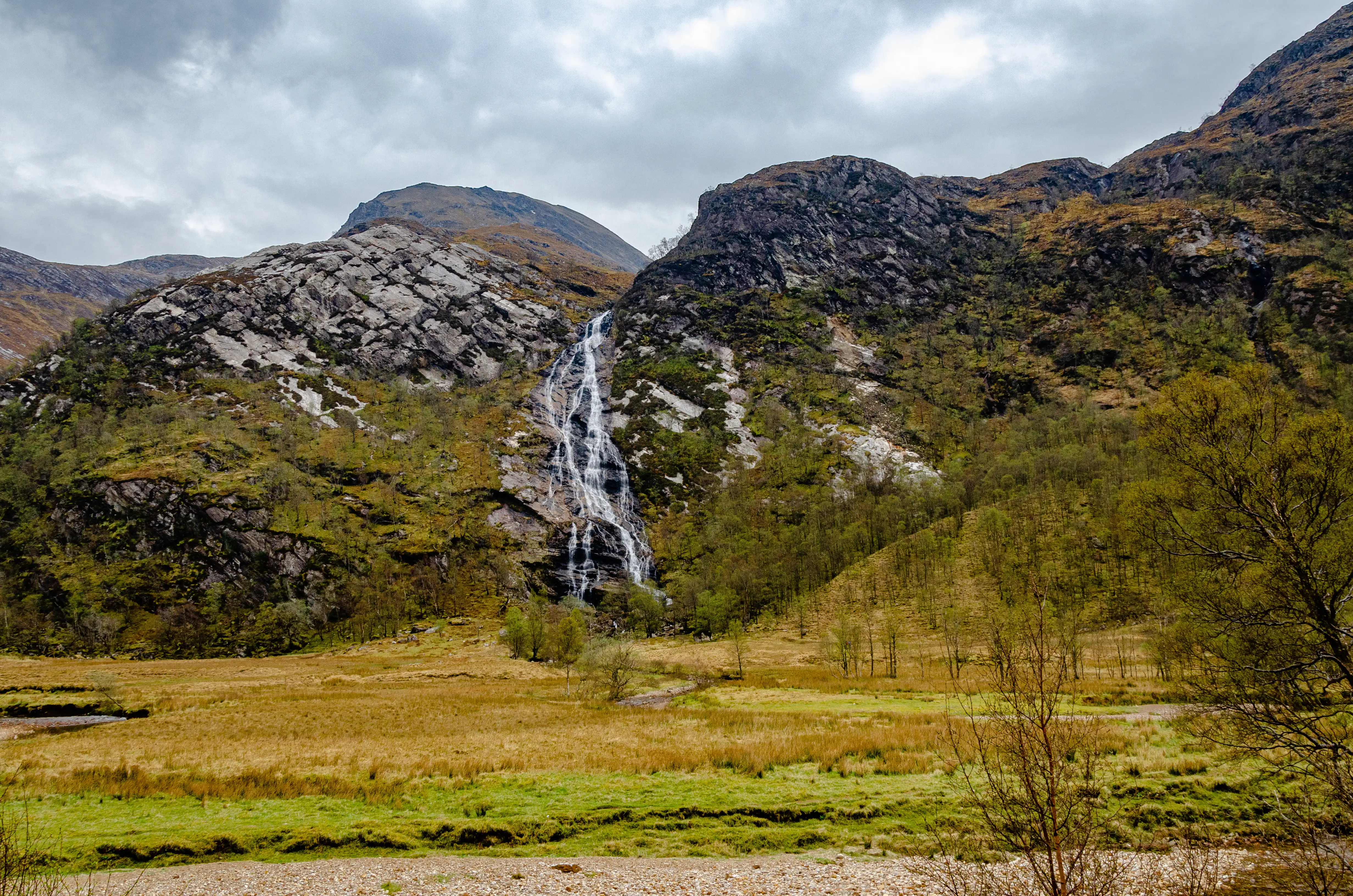 Uitzicht op de Steall Falls in Schotland, met water dat langs een rotsachtige klif naar beneden klettert, omzoomd door groen en bergen.