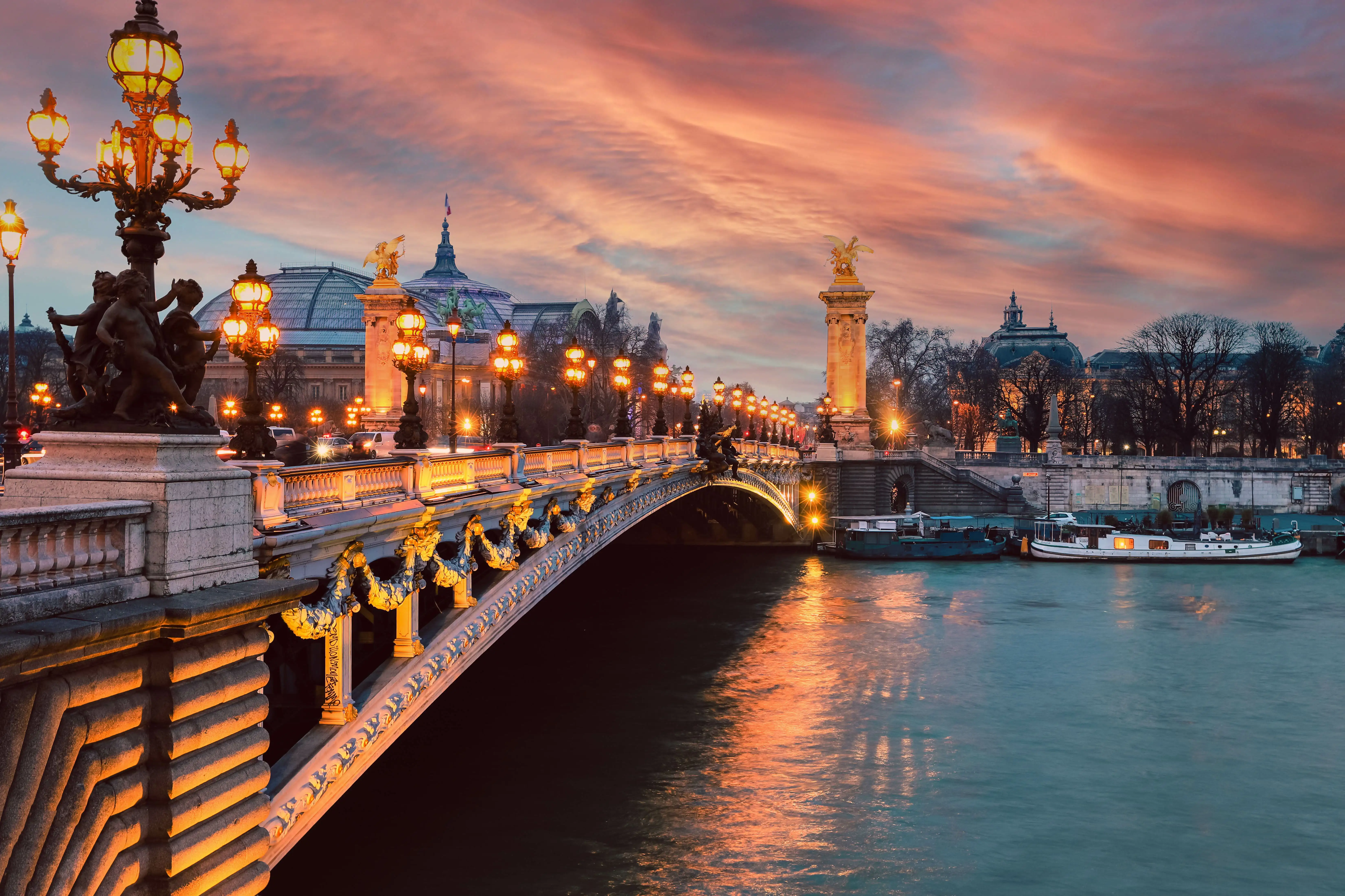Pont Alexandre III bridge over the River Seine in Paris in the evening, illuminated with lights under a pink sky.
