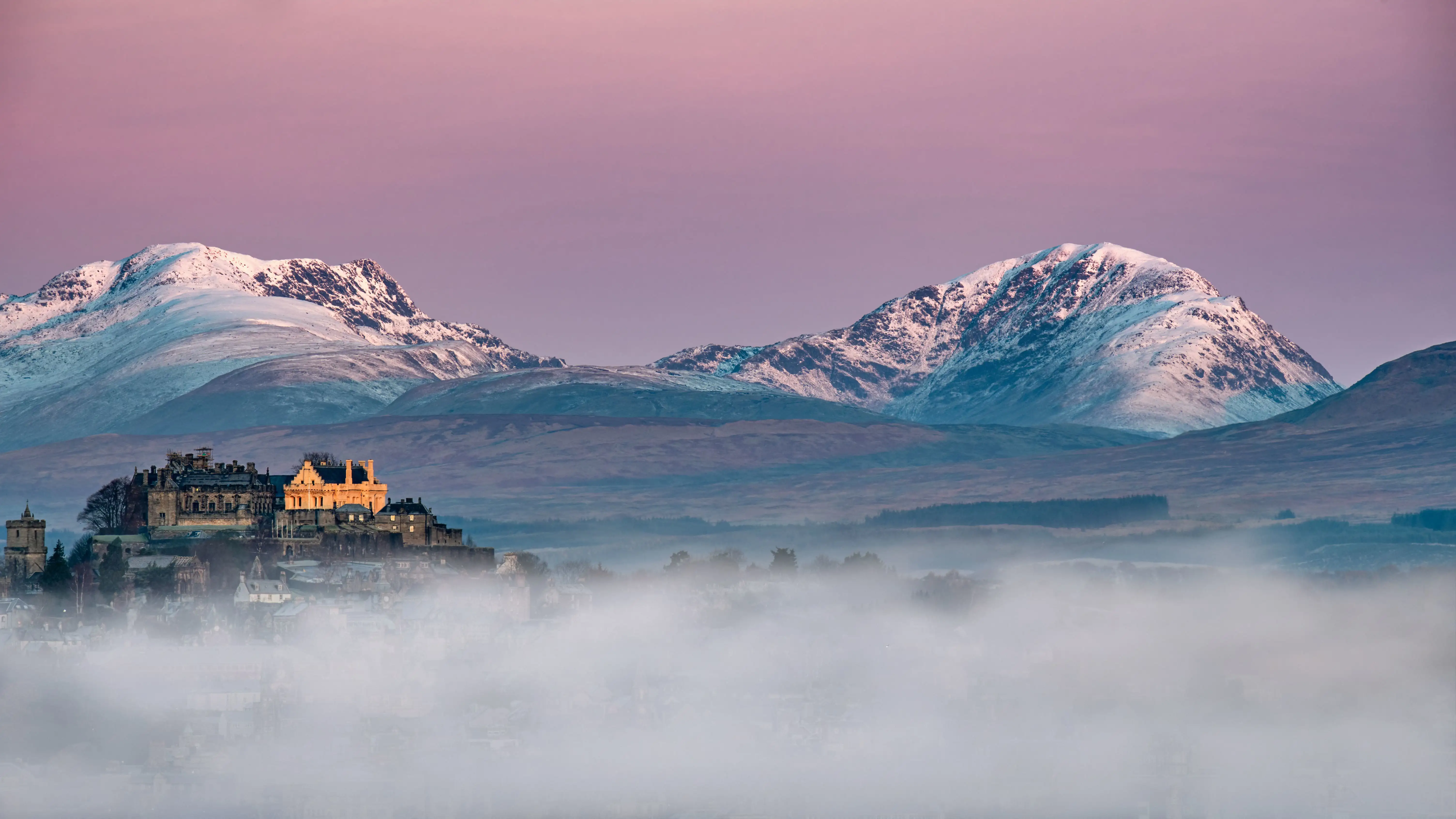 Een mistige zonsopgang met besneeuwde bergtoppen bij Stirling Castle in Schotland.