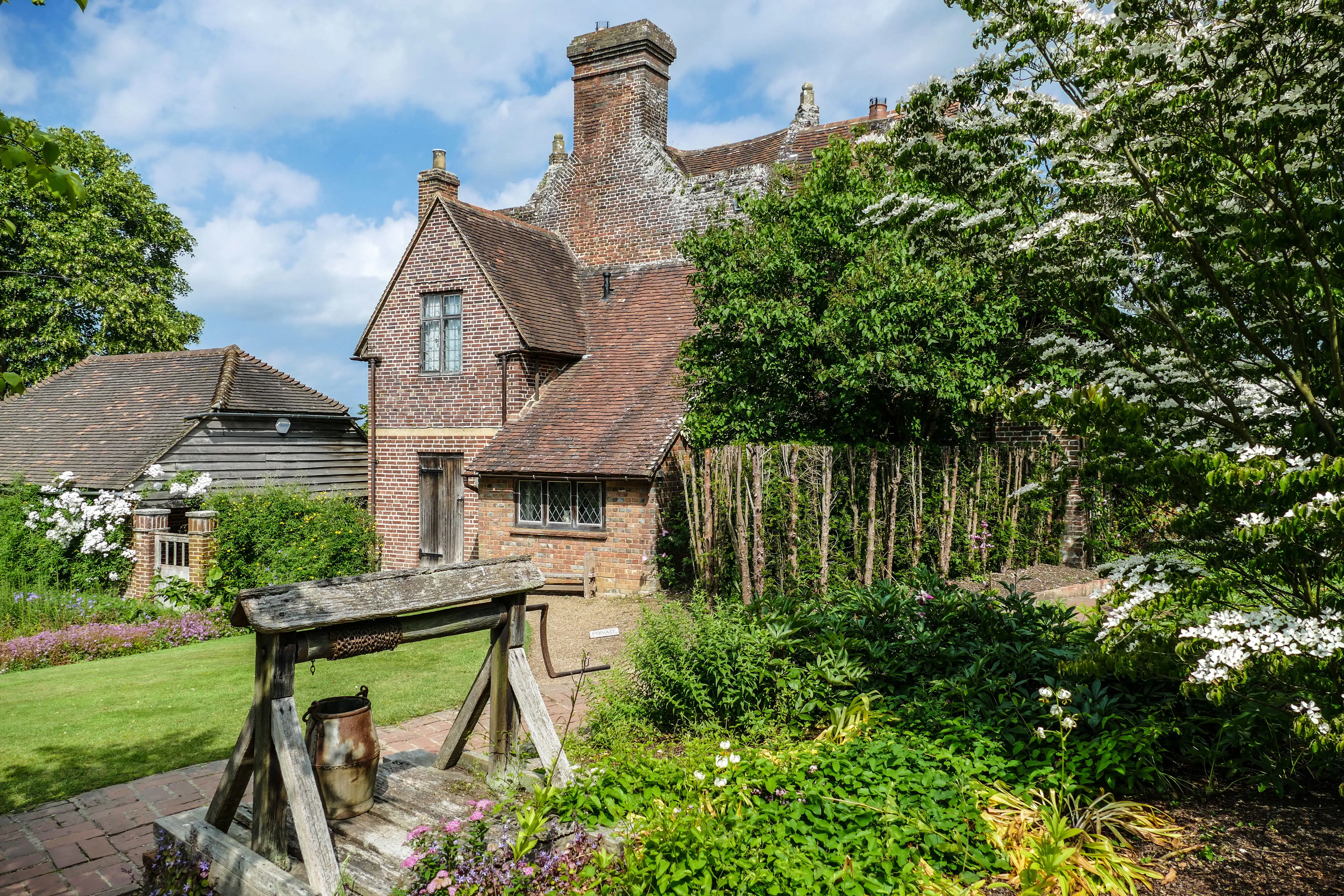 Les jardins du château de Sissinghurst dans le Kent en Angleterre avec de la végétation luxuriante, des fleurs colorées et un domaine historique en toile de fond.
