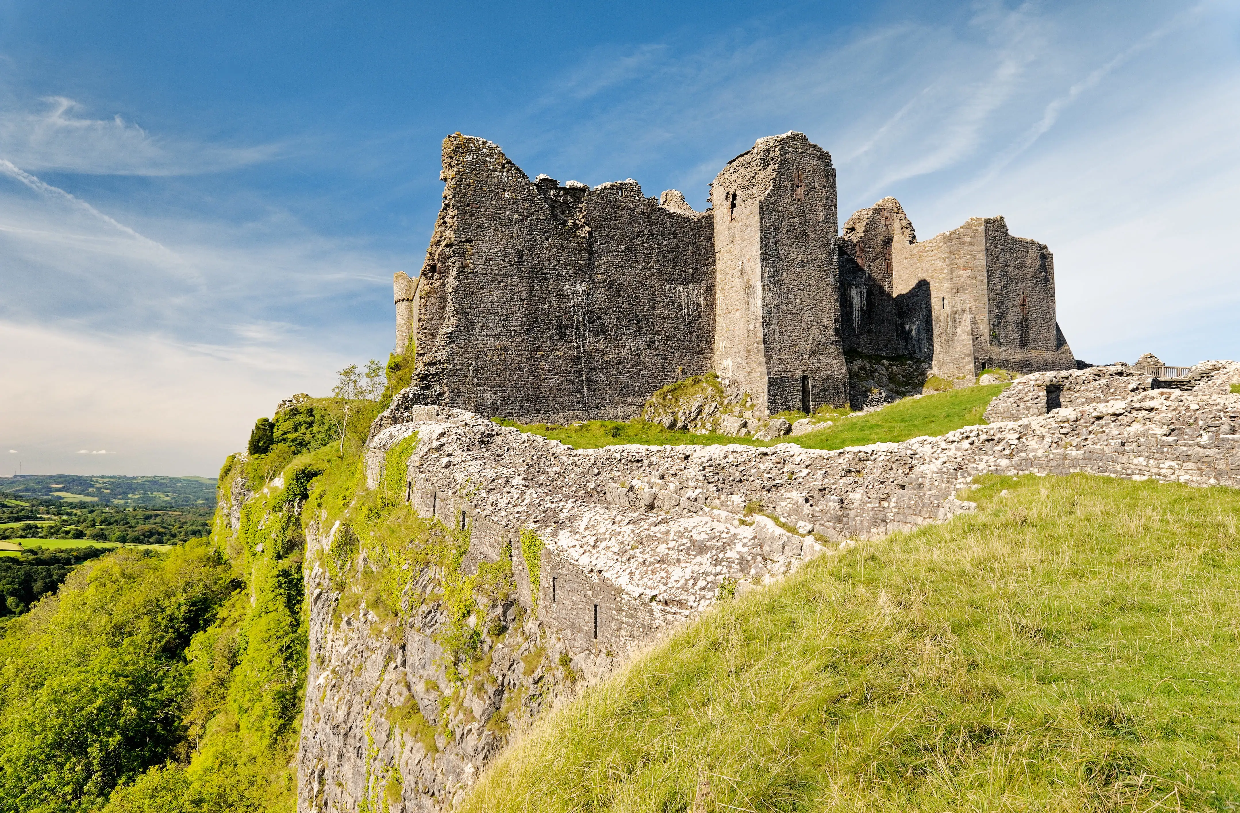Kasteel Carreg Cennen op een kalkstenen klif onder een helderblauwe hemel overdag.
