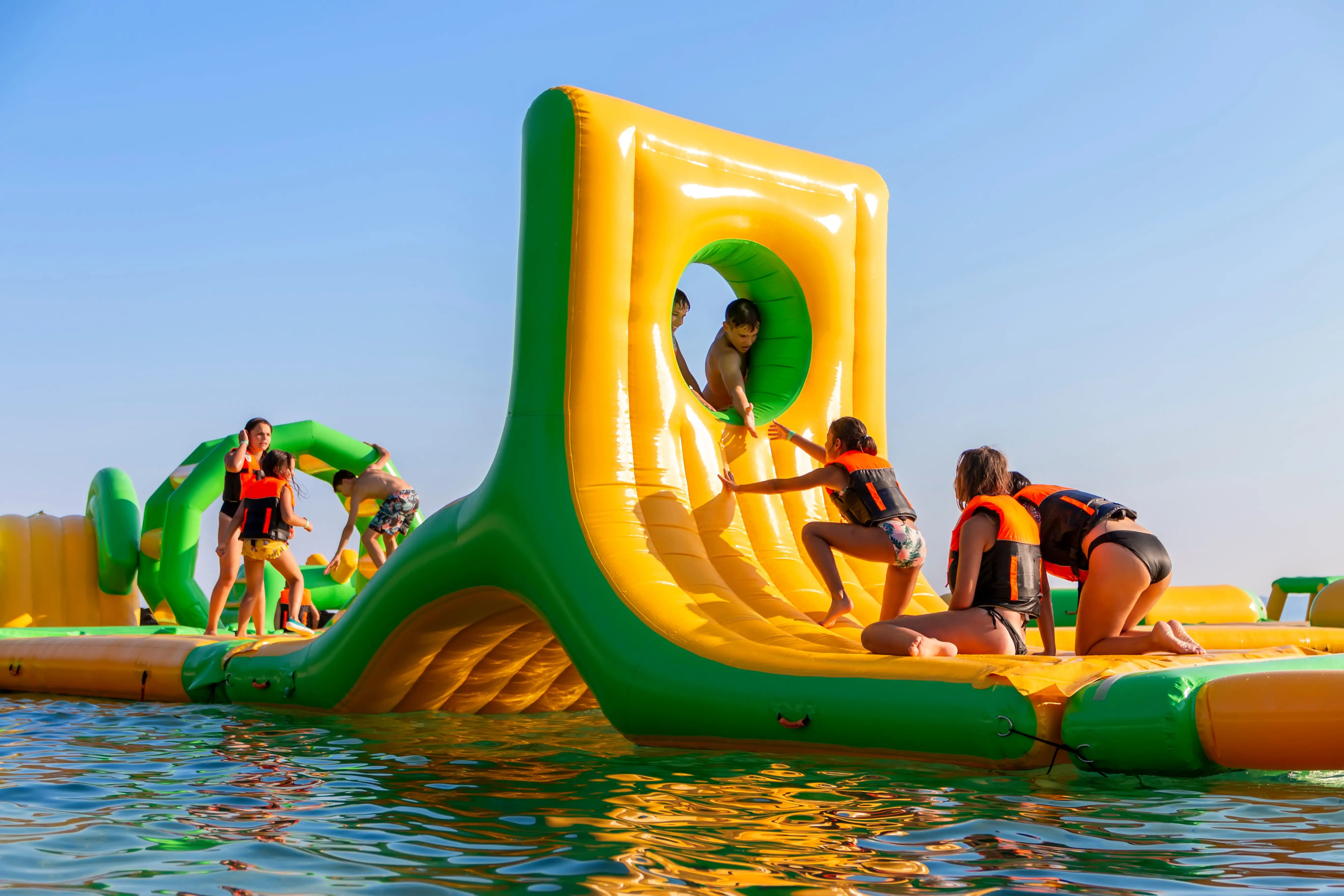 People climbing through a colourful, inflatable obstacle course on the water.