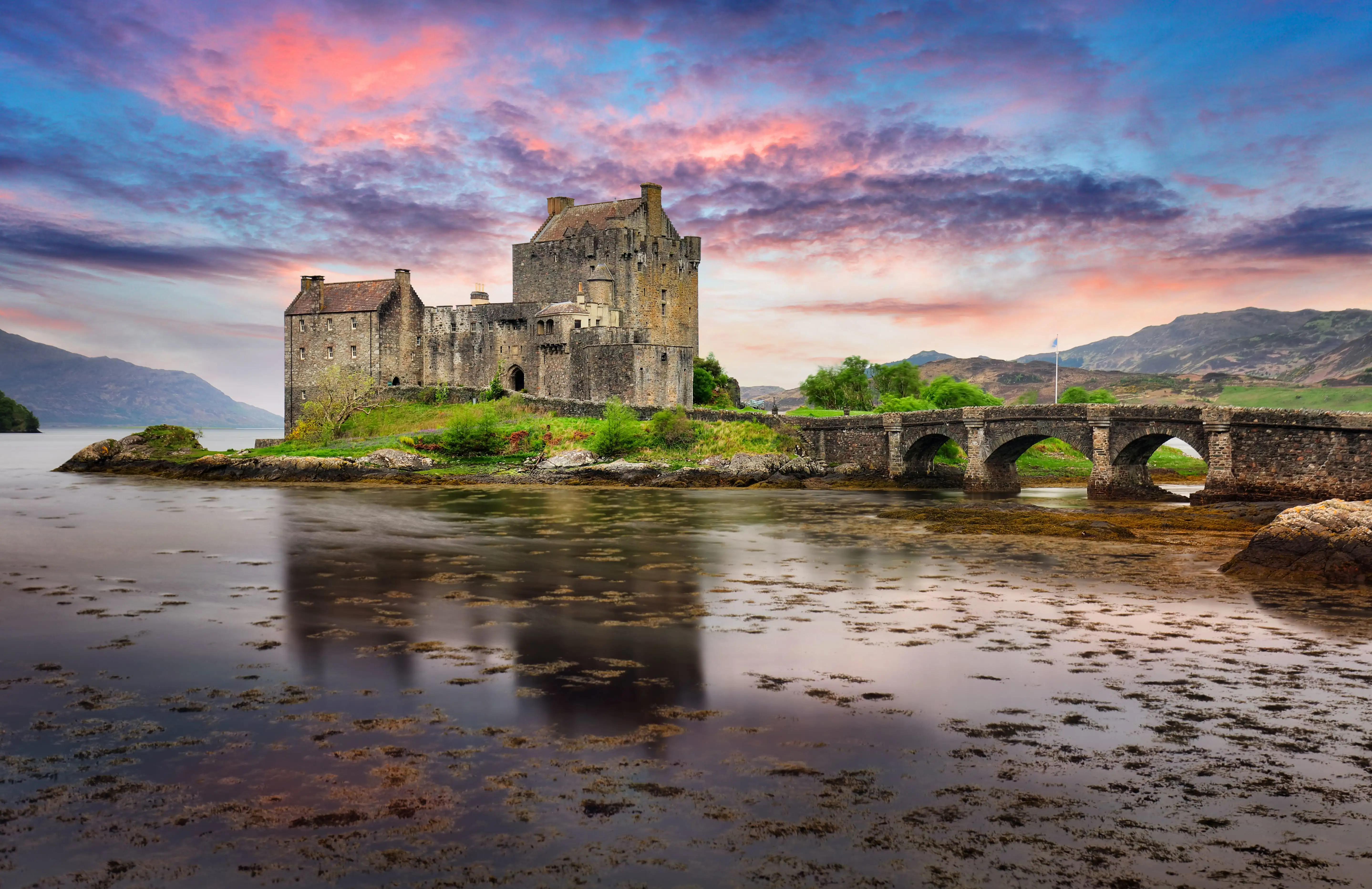Le château d’Eilean Donan au coucher du soleil, avec un ciel rose et violet.