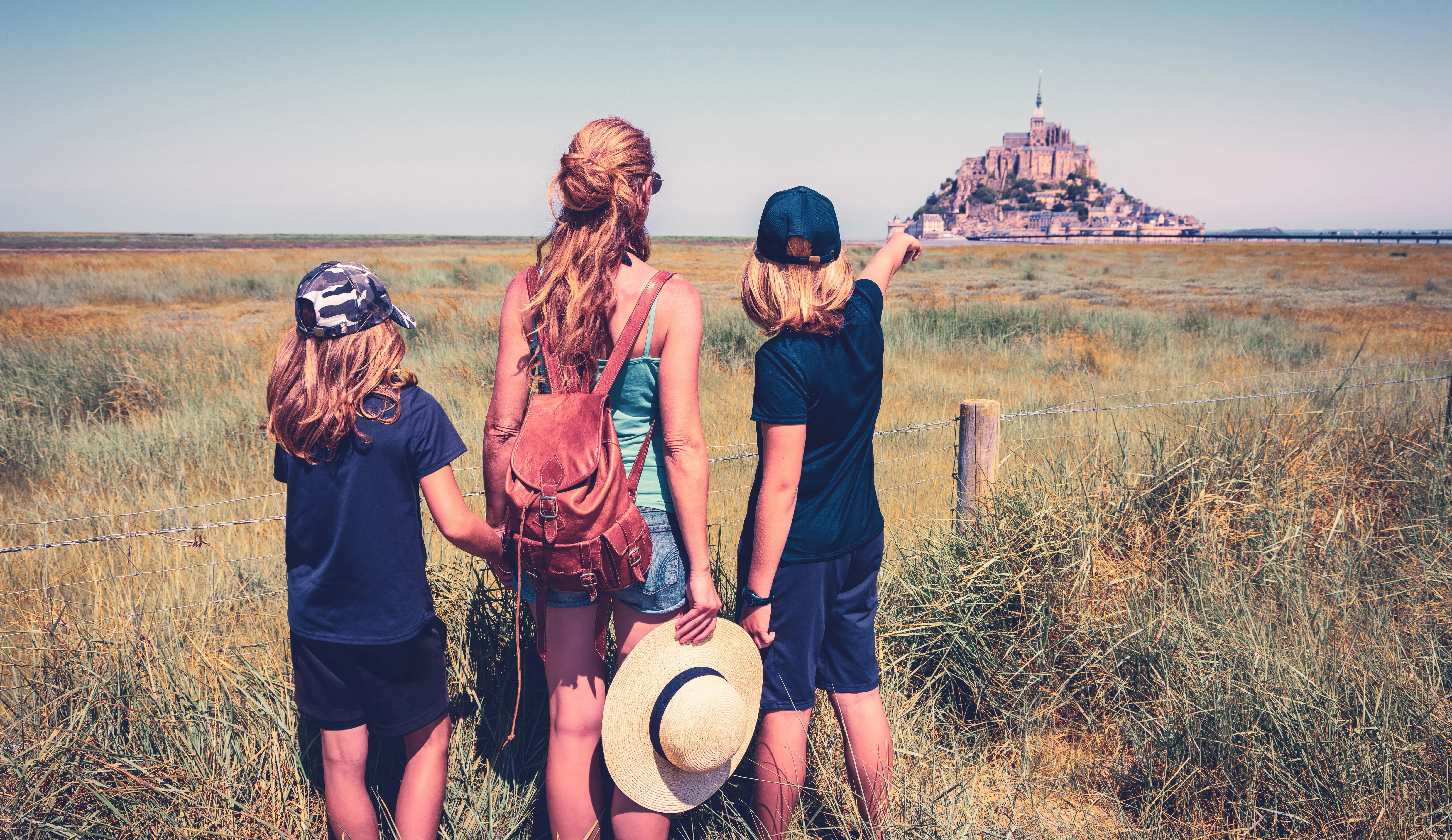 Family of three seen from behind, looking at Mont Saint-Michel in Normandy, France, from a distance on a family holiday.