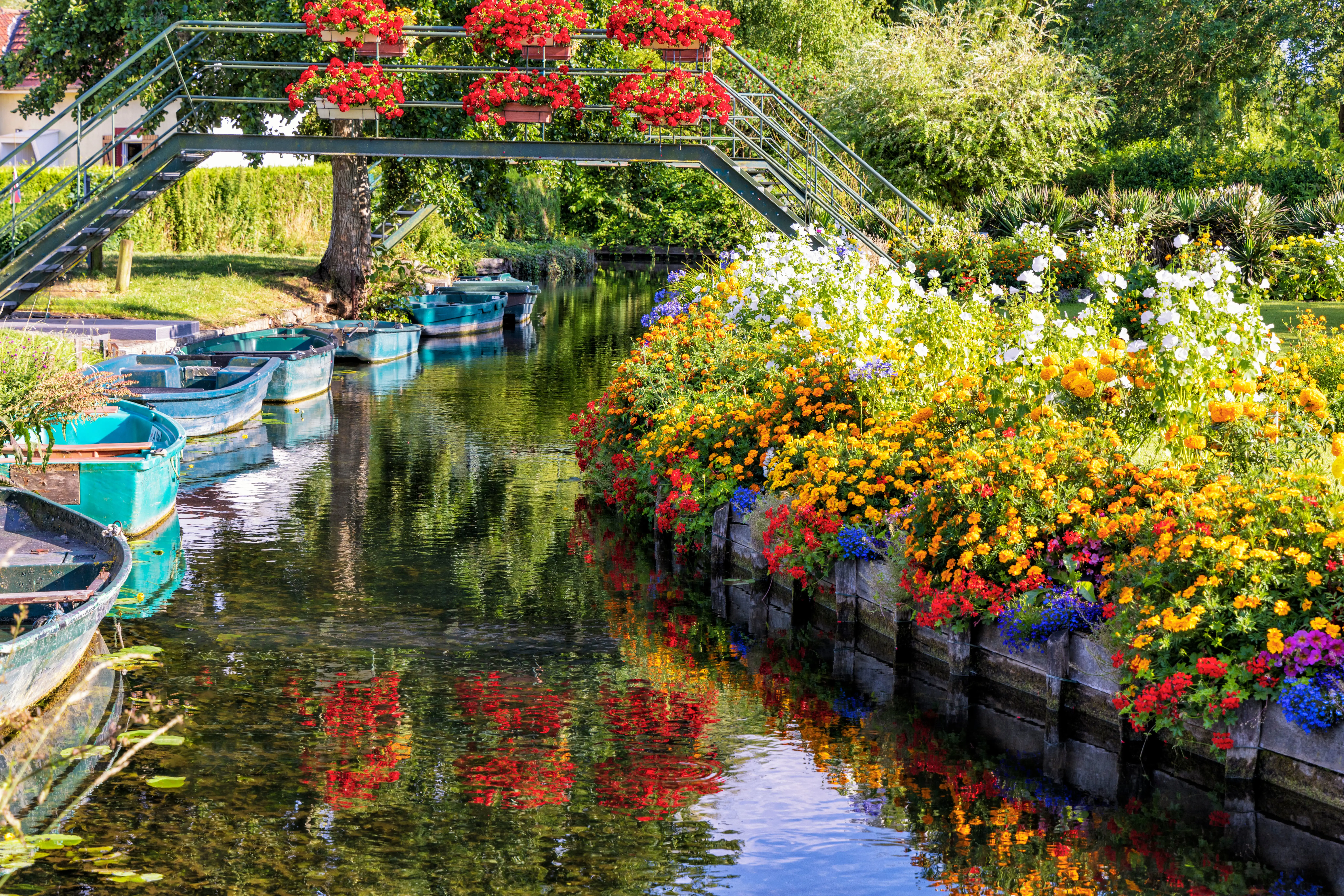 Boats moored along the canals of the Hortillonnages in Amiens, with colourful flowers reflected in the calm water.