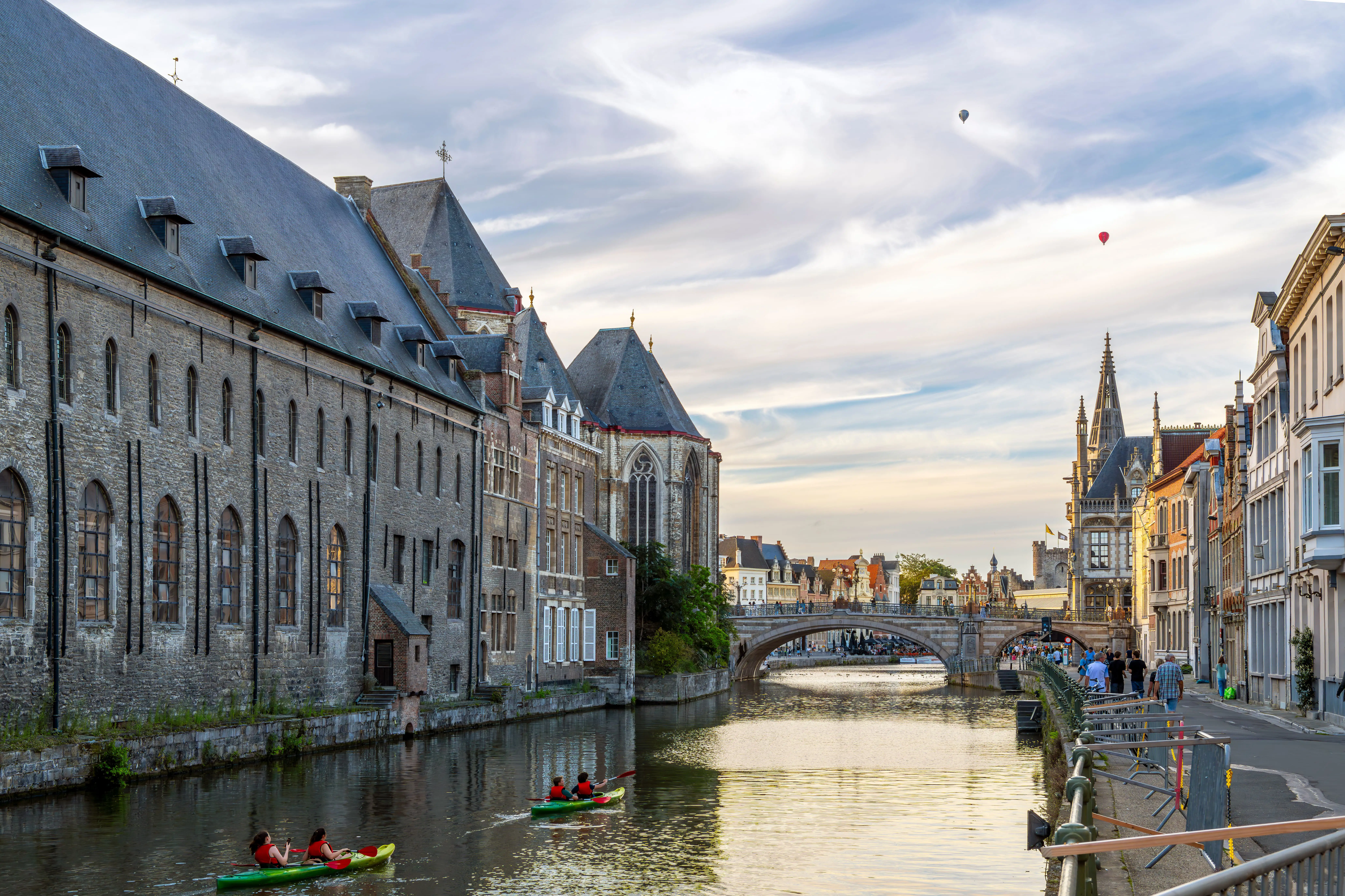 Kayakers paddling through Ghent, Belgium at twilight with historic buildings lit up along the canal.
