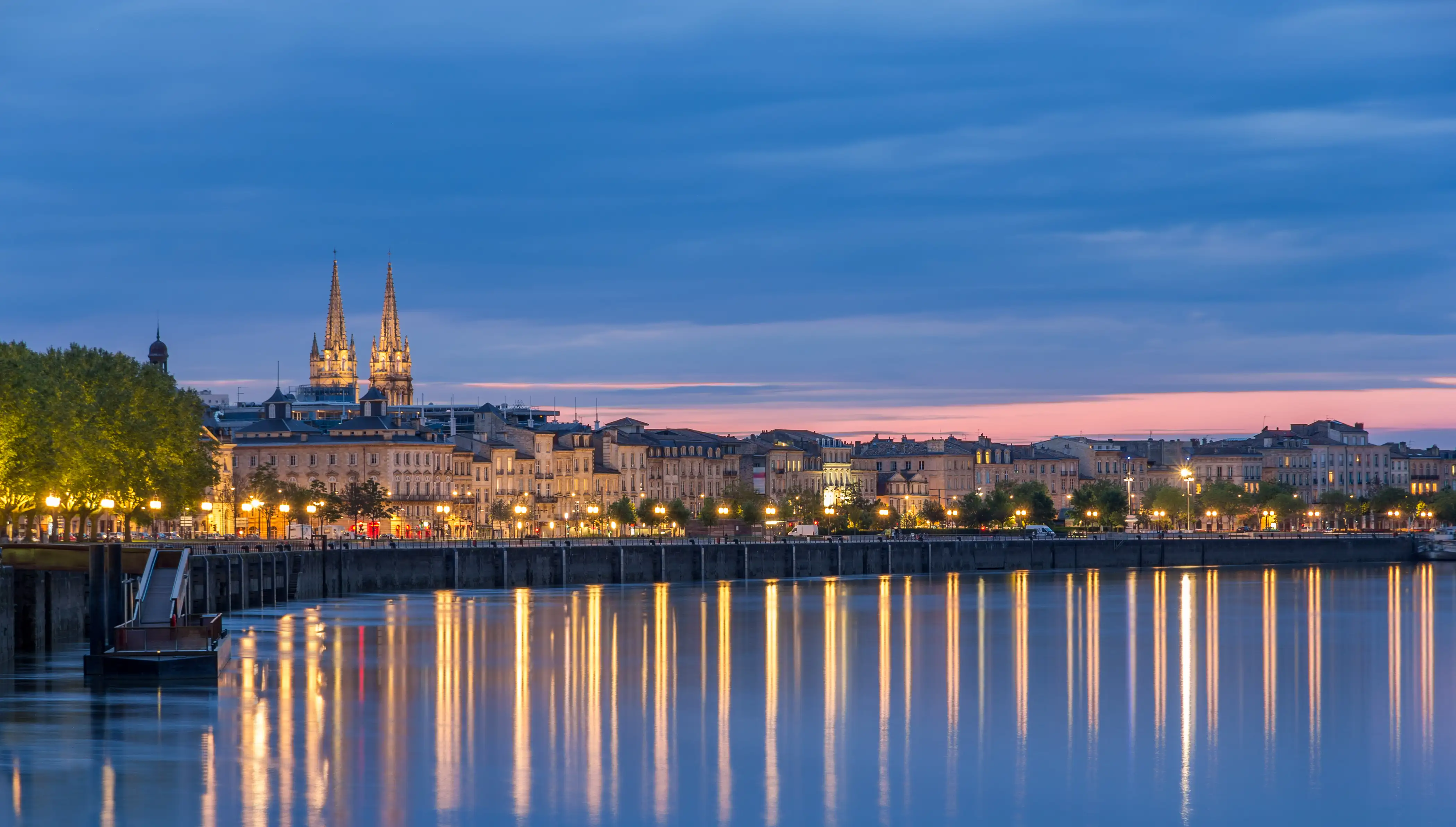 Evening view of Bordeaux’s illuminated riverfront with reflections on the Garonne River.