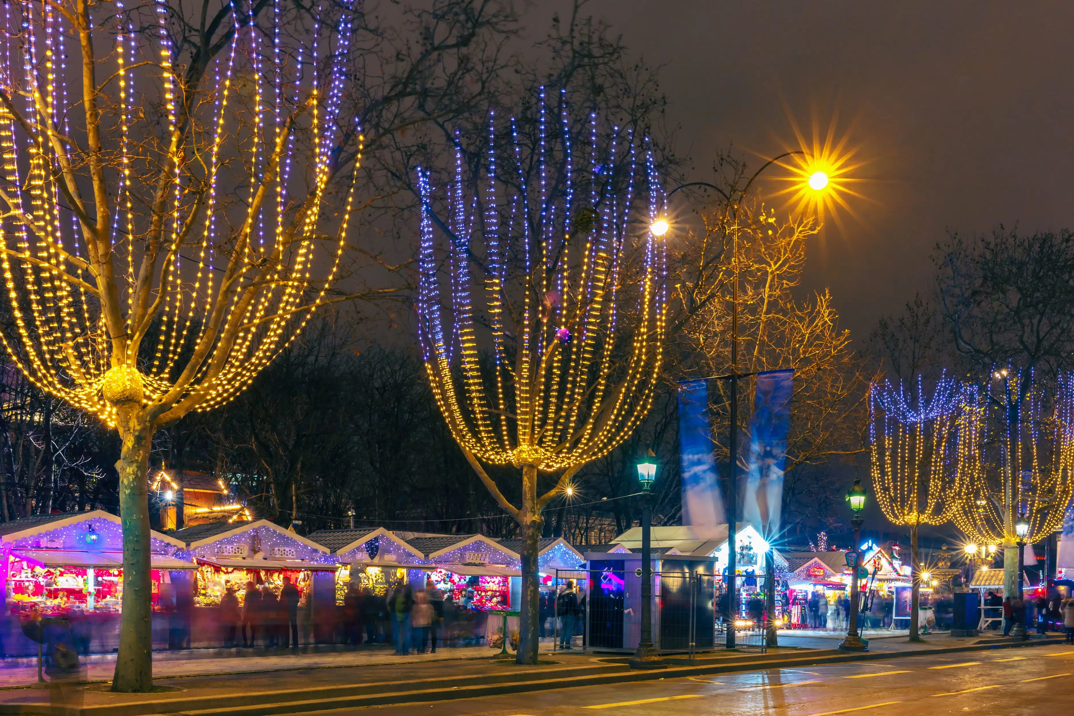 Nighttime view of the Christmas market on the Champs-Élysées in Paris, with illuminated trees and festive lights.