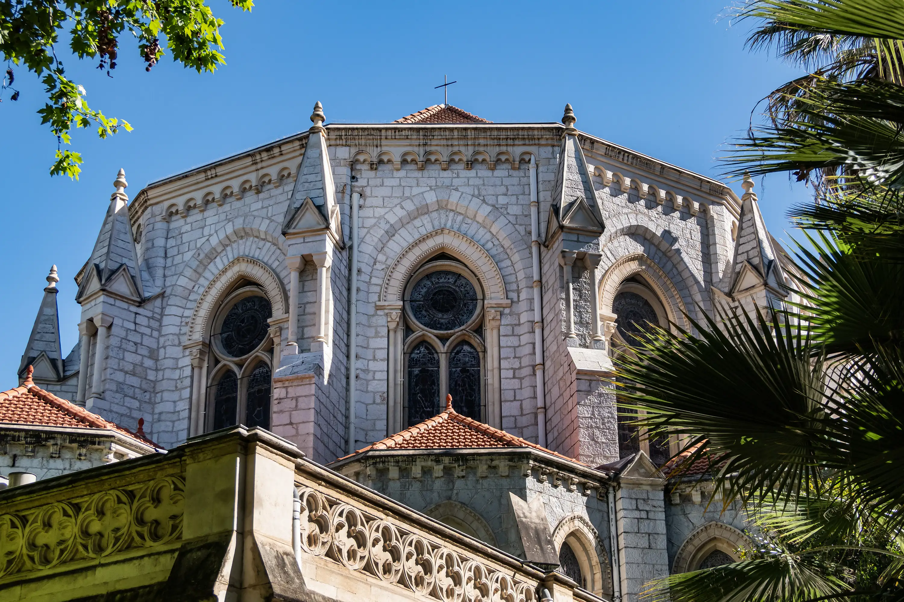 Close-up view of three ornate stained-glass windows on the facade of the Basilica of Notre-Dame de Nice against a bright blue sky.