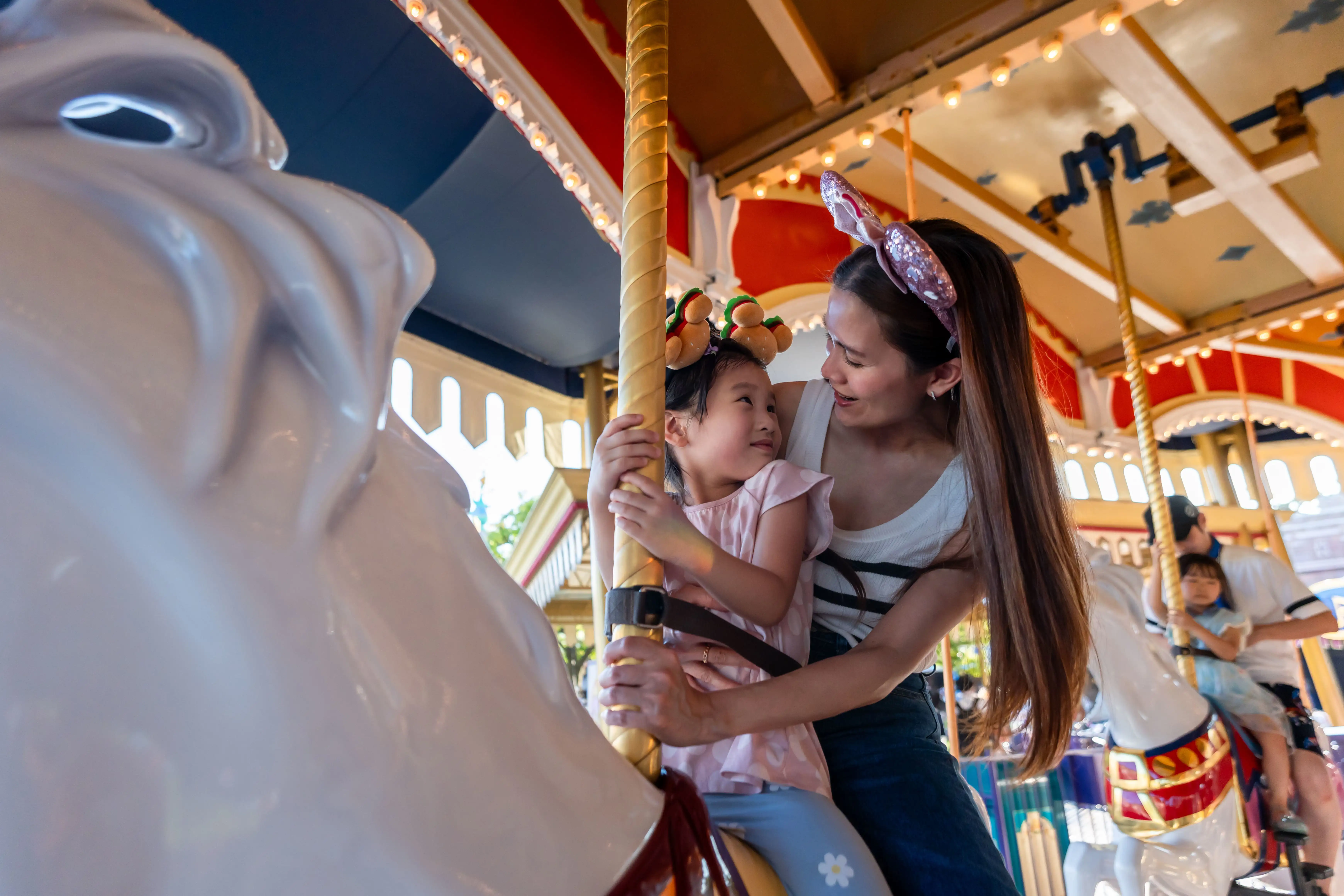Mother and child smiling while riding a carousel at a theme park.