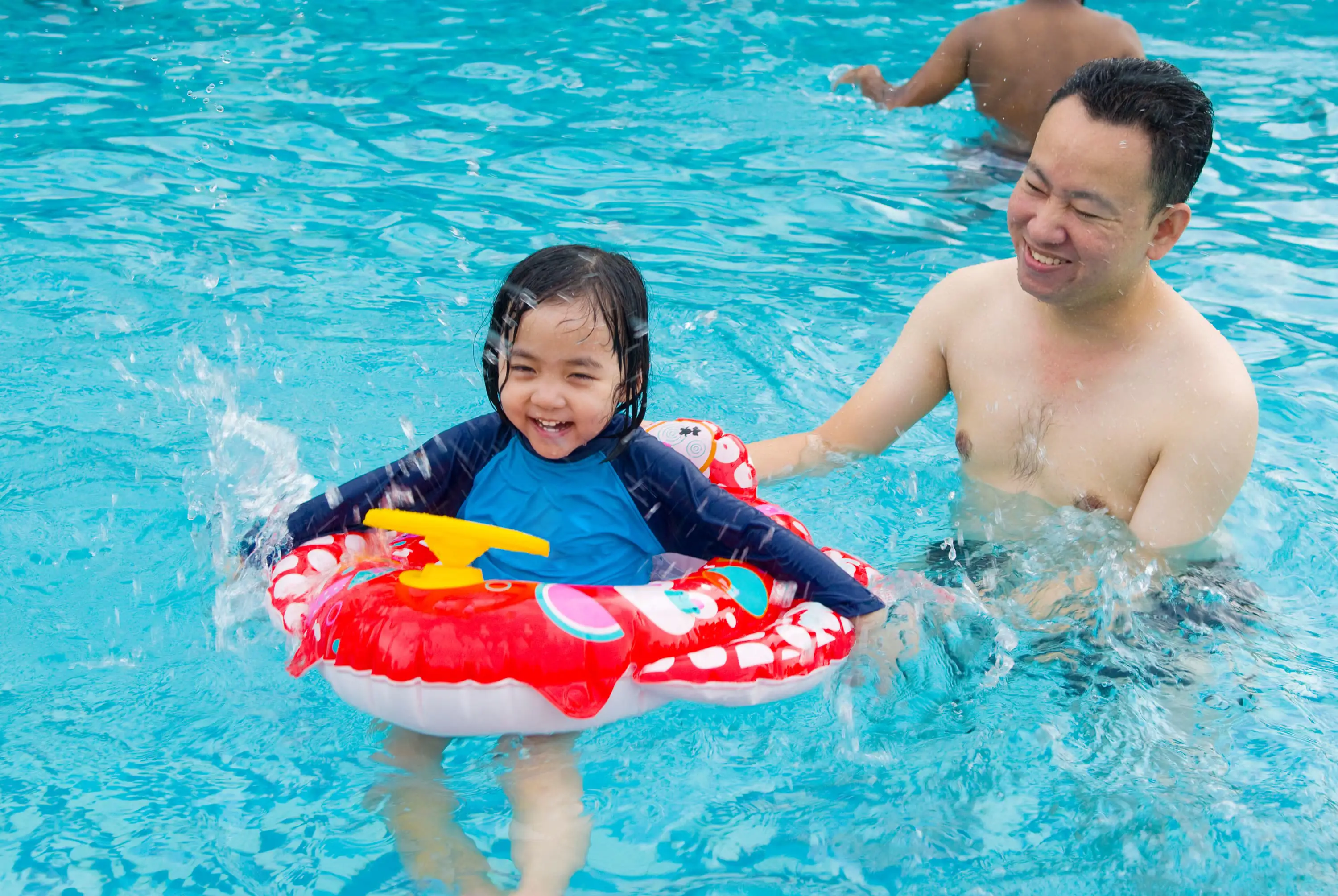 Father and daughter play in the water with an inflatable.
