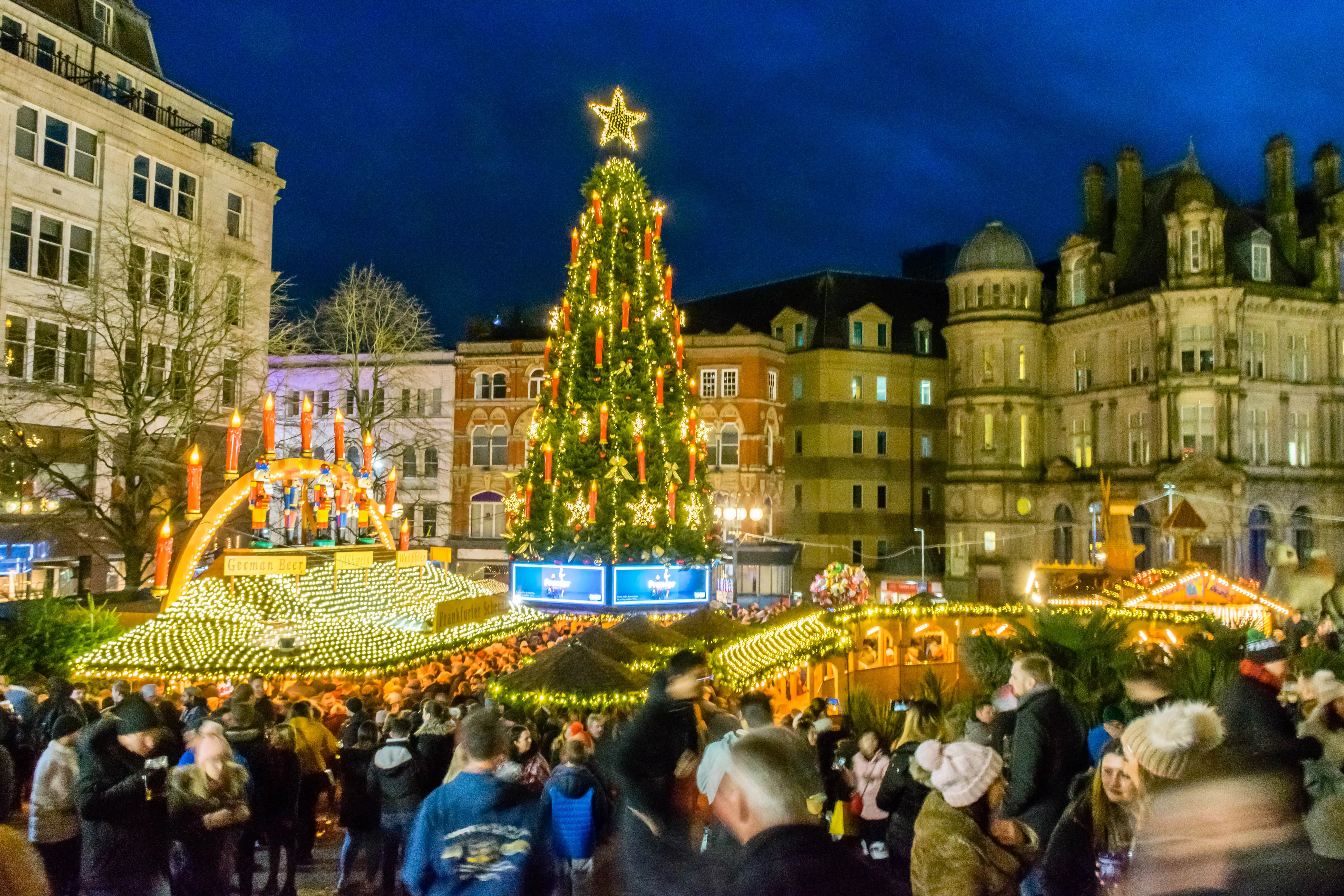 Kerstmarkt in het centrum van Birmingham in de avond met verlichte kraampjes en een feestelijke drukte.