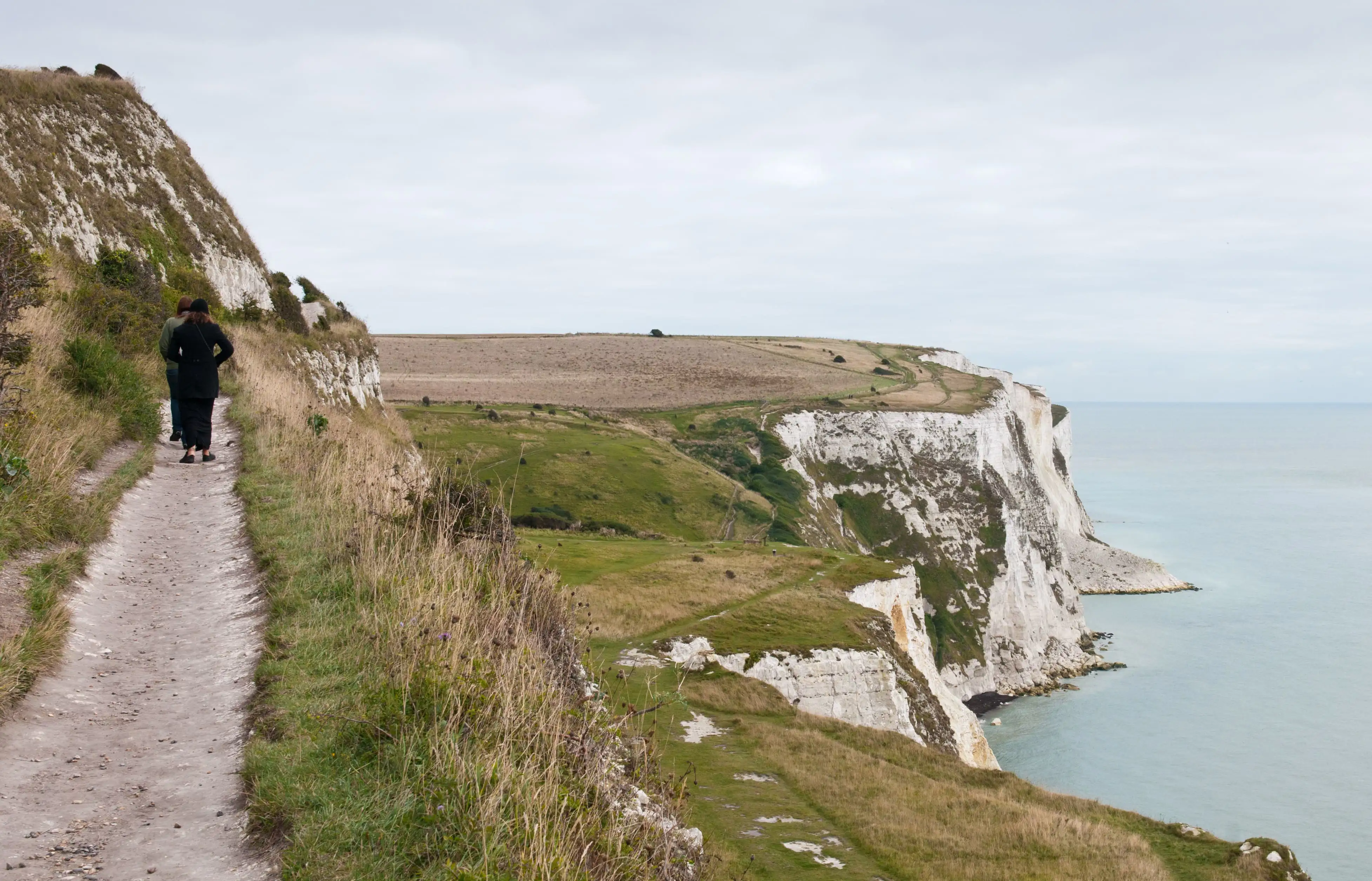 Mensen lopen over de krijtrotsen bij Dover op een bewolkte herfstdag met uitzicht op de Noordzee.
