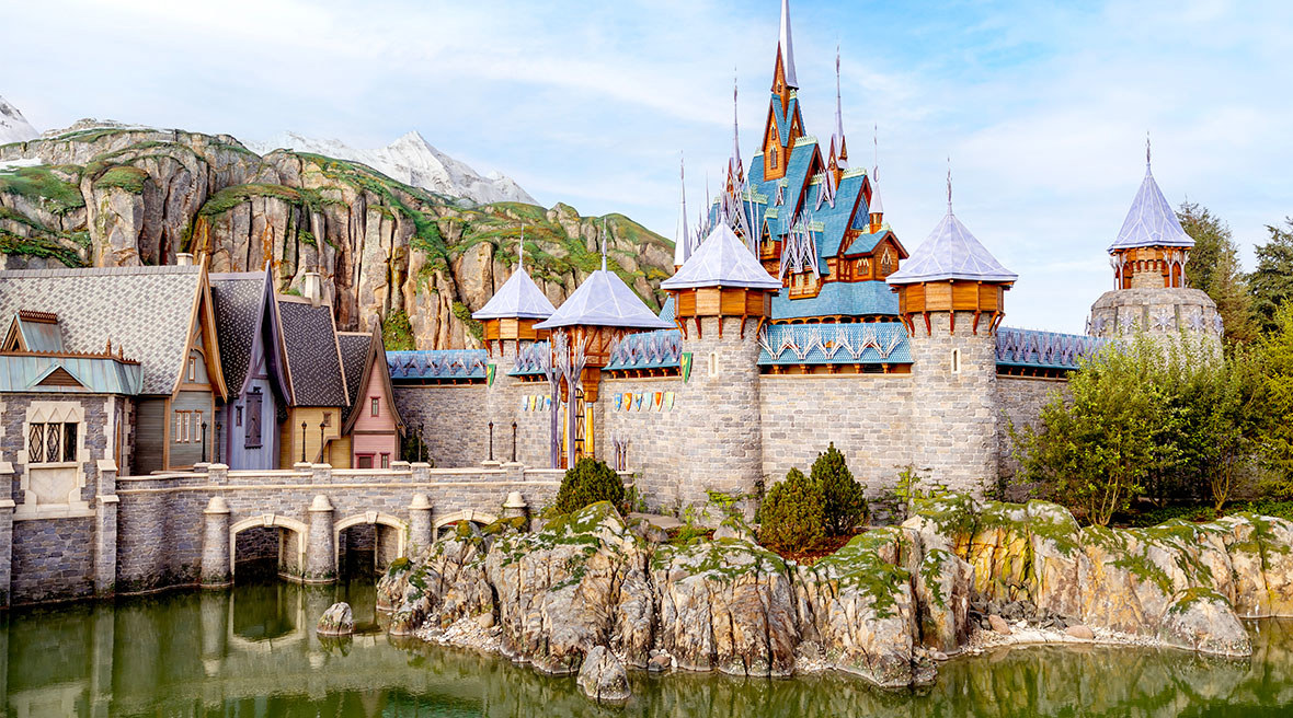 A panoramic view of the rugged mountain terrain and the crystalline structure of the Ice Palace overlooking the Arendelle waterfront.