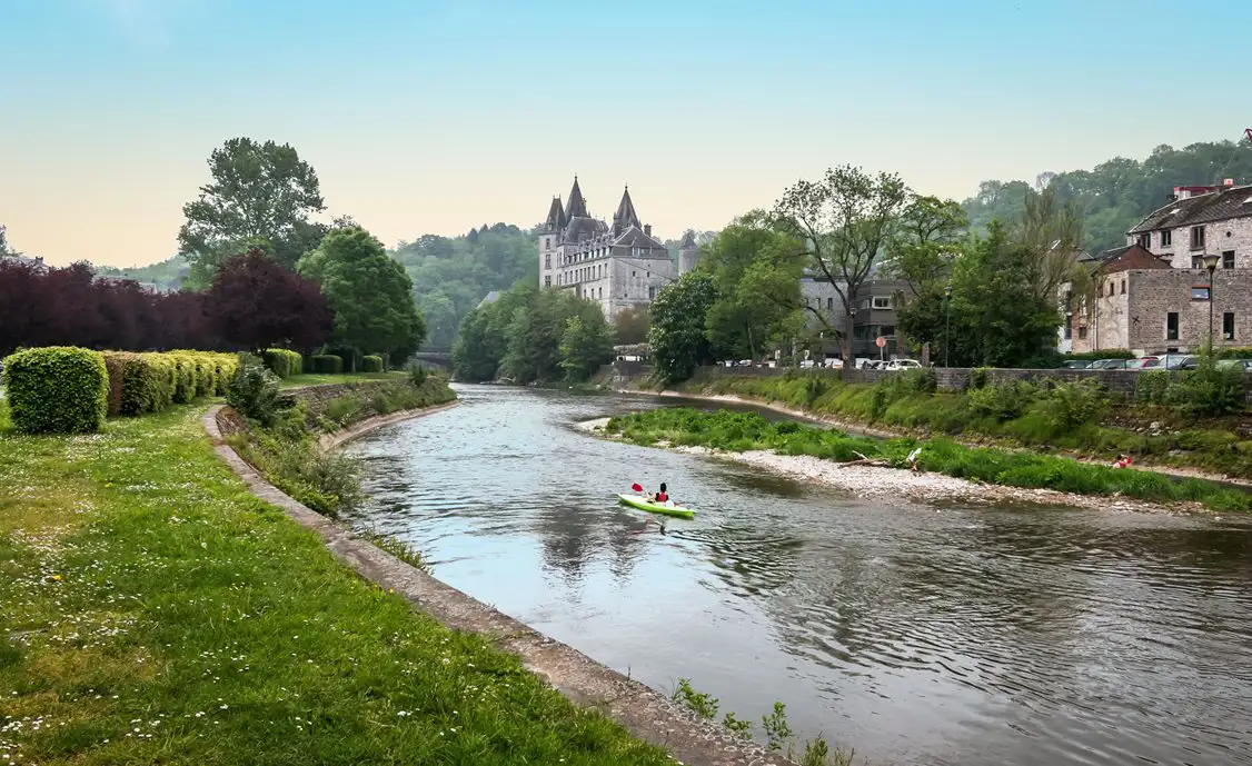 Someone kayaking down the Ourthe river with Durbuy castle in the background