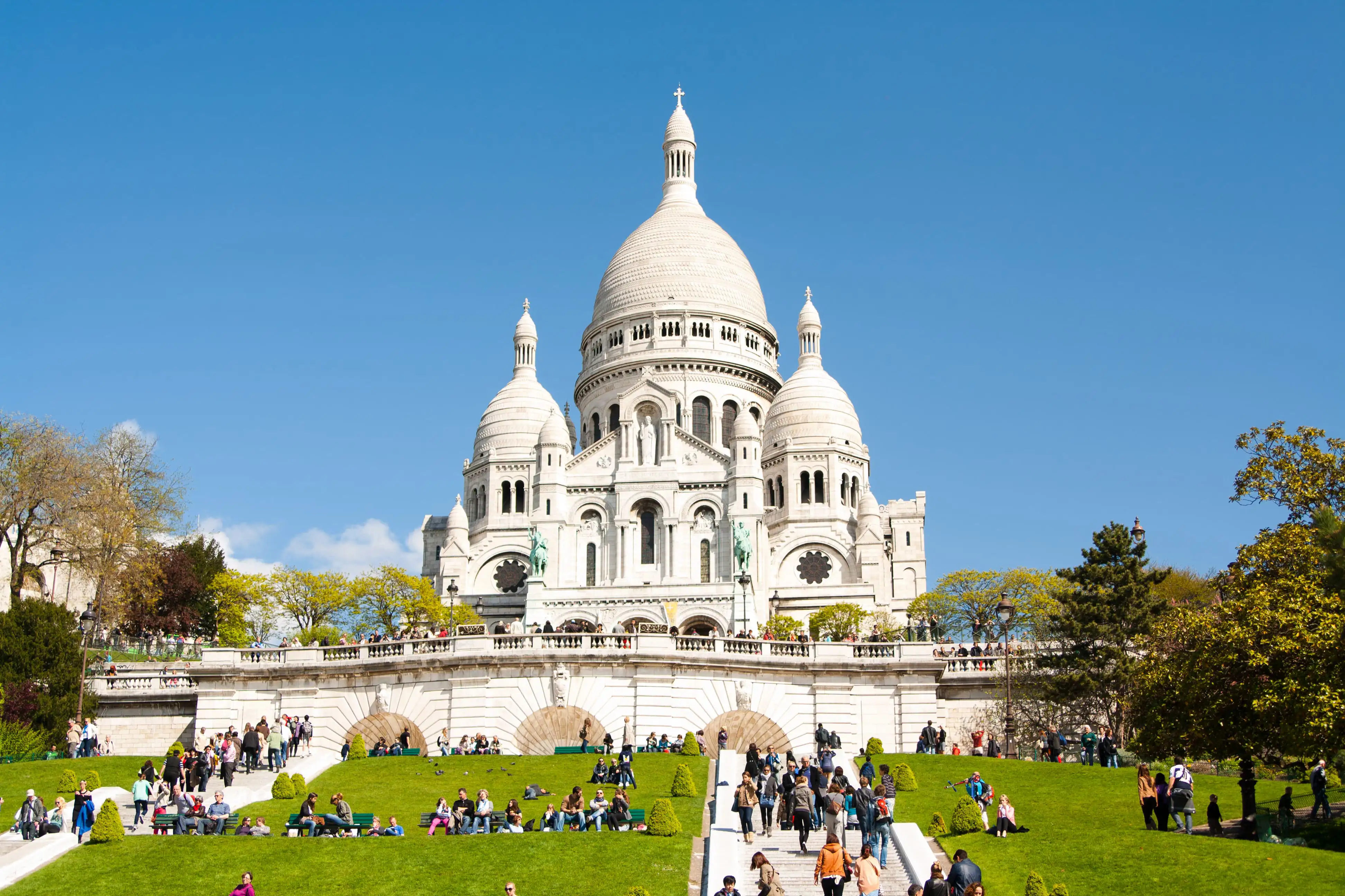 Sacré-Cœur Basilica in Paris on a sunny day with blue skies and crowds of visitors on the steps