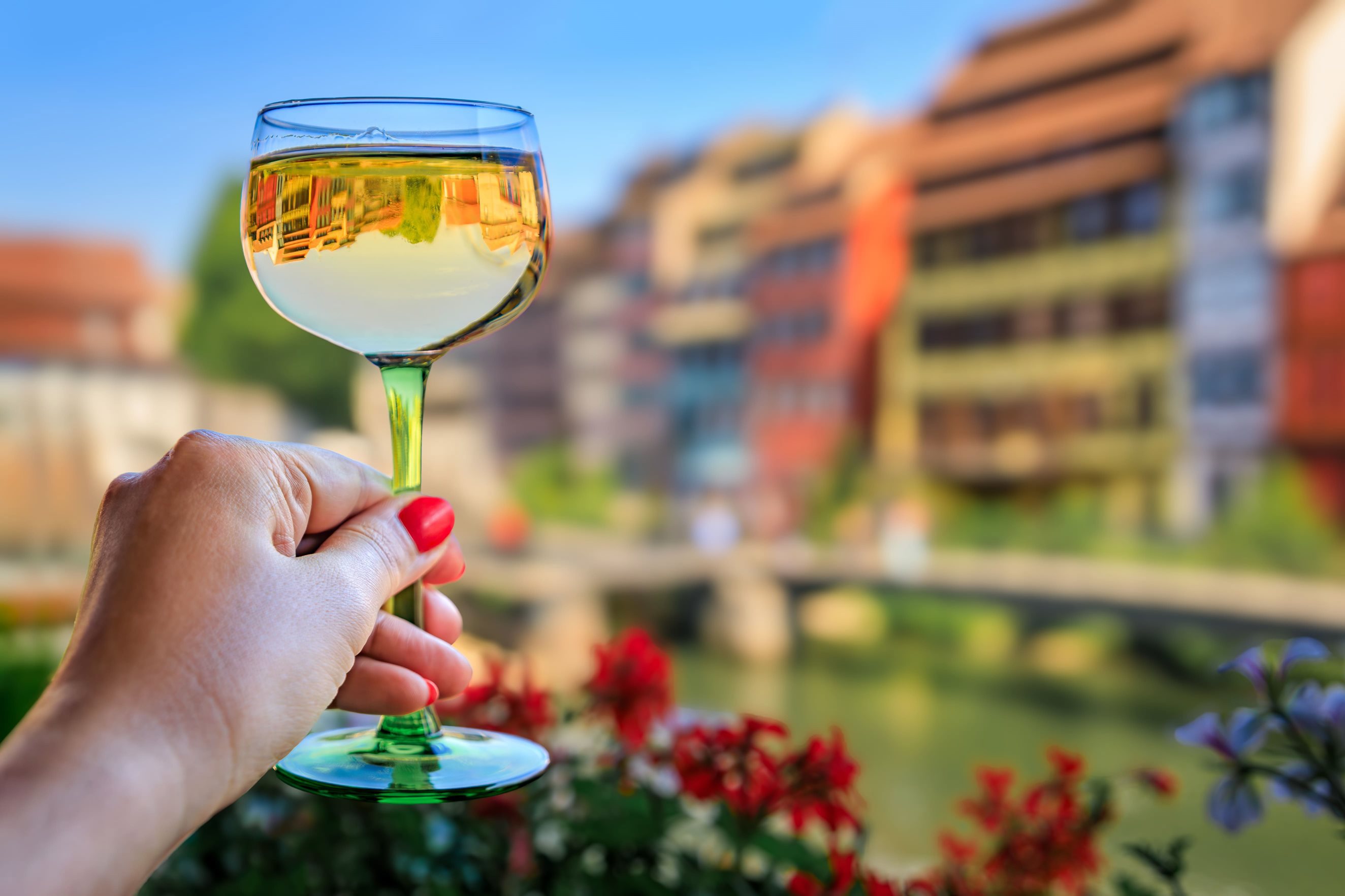 Woman’s hand holding a glass of white win up before a blurred out city background