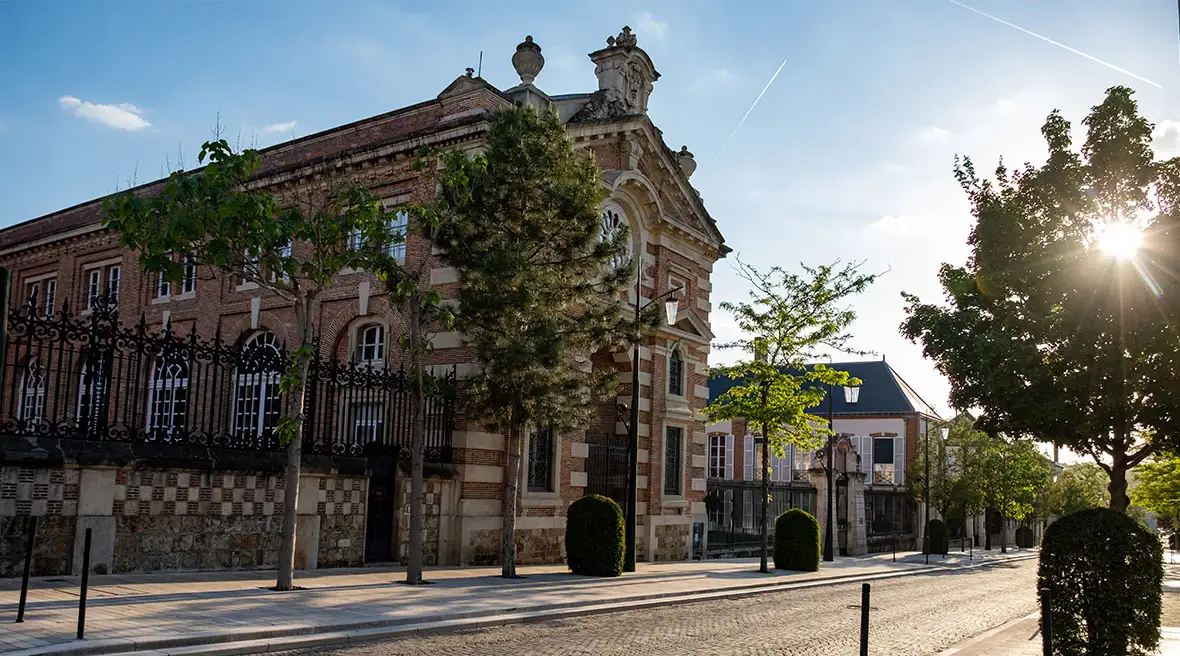 an historic brick champagne house with an ornate facade and a cobblestone street lined with trees