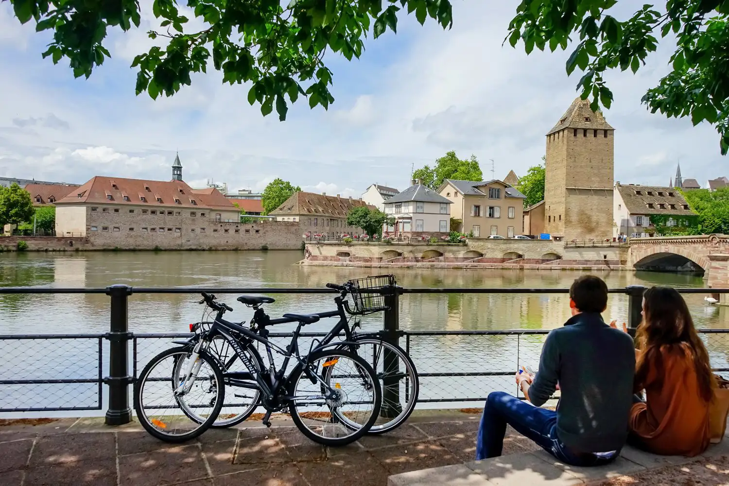 A young couple looking across at Barrage Vauban in Strasbourg, with their bikes parked