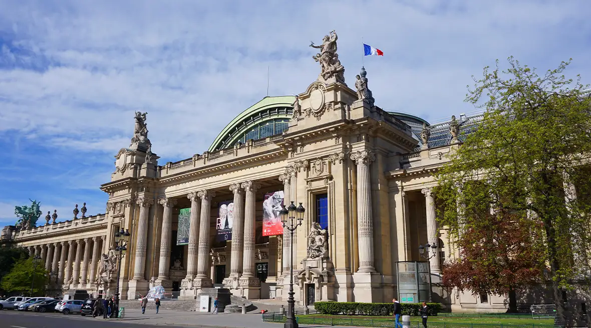 The frontage of the Grand Palais in Paris on a sunny day, with a French flag flying from the top of the building.