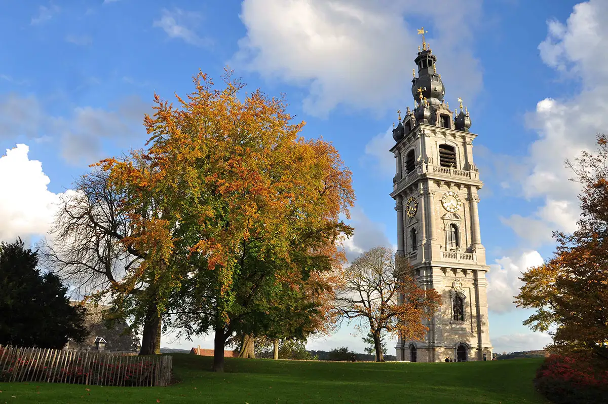 A beautiful stone belfry rising above greenery with a large tree to the left