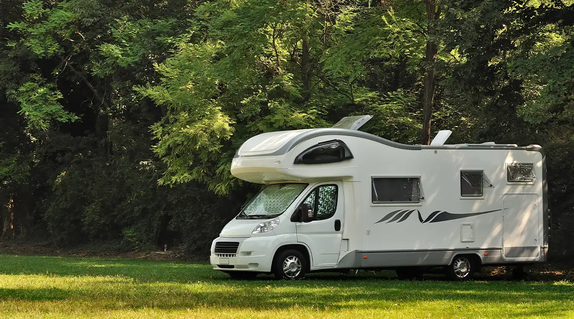 A large white, coachbuilt motorhome with overhang sleeping area above the cab. Set in a green field
