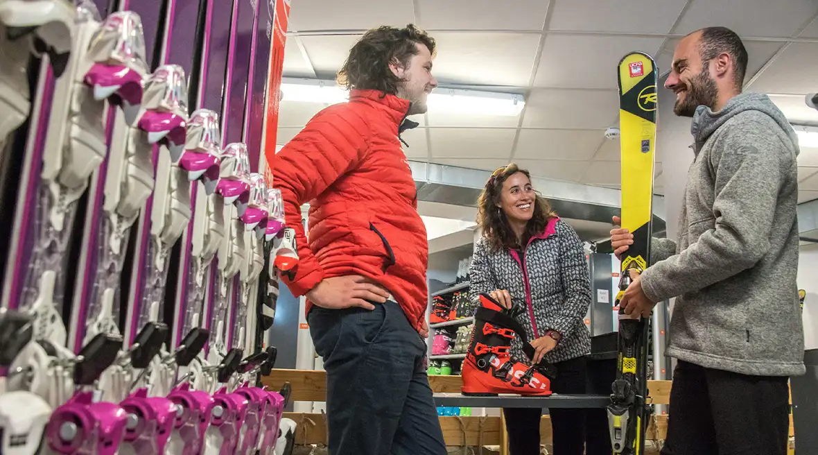 Two men and a woman in the ski boot fitting room. A row of red skis in the foregrounds
