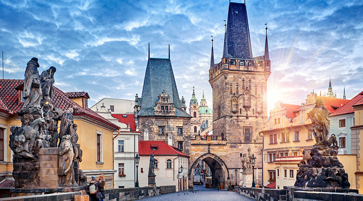 sun setting behind beautiful old buildings in a town square with statues in the foreground