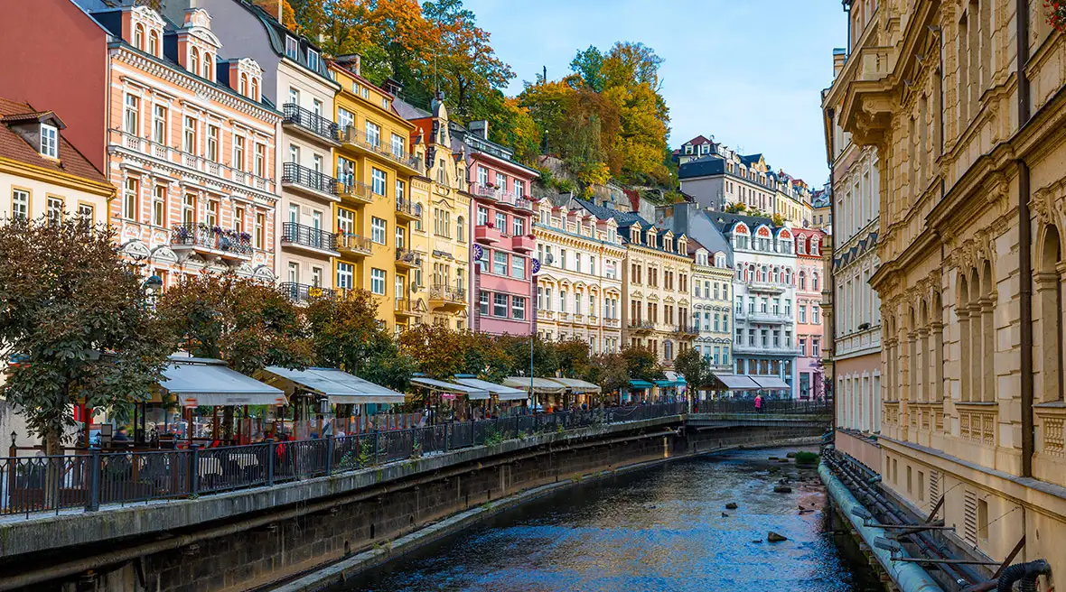 A line of colourful buildings in yellows pinks and reds along the banks of a river