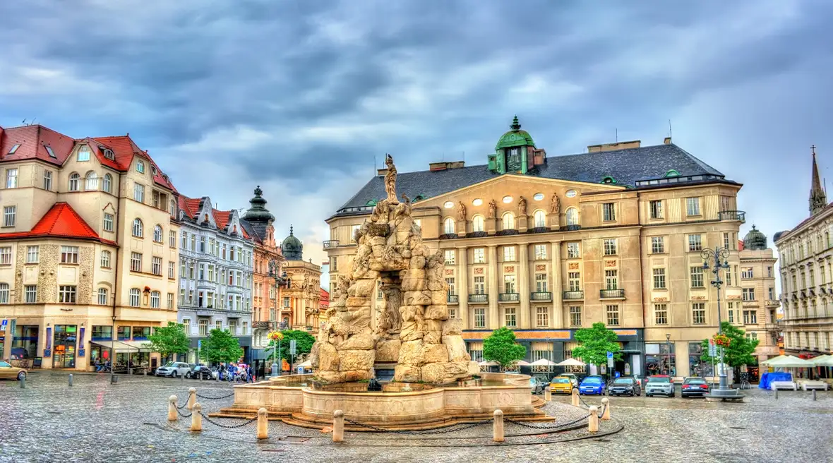 A large stone fountain in the middle of a town square surrounded by baroque buildings