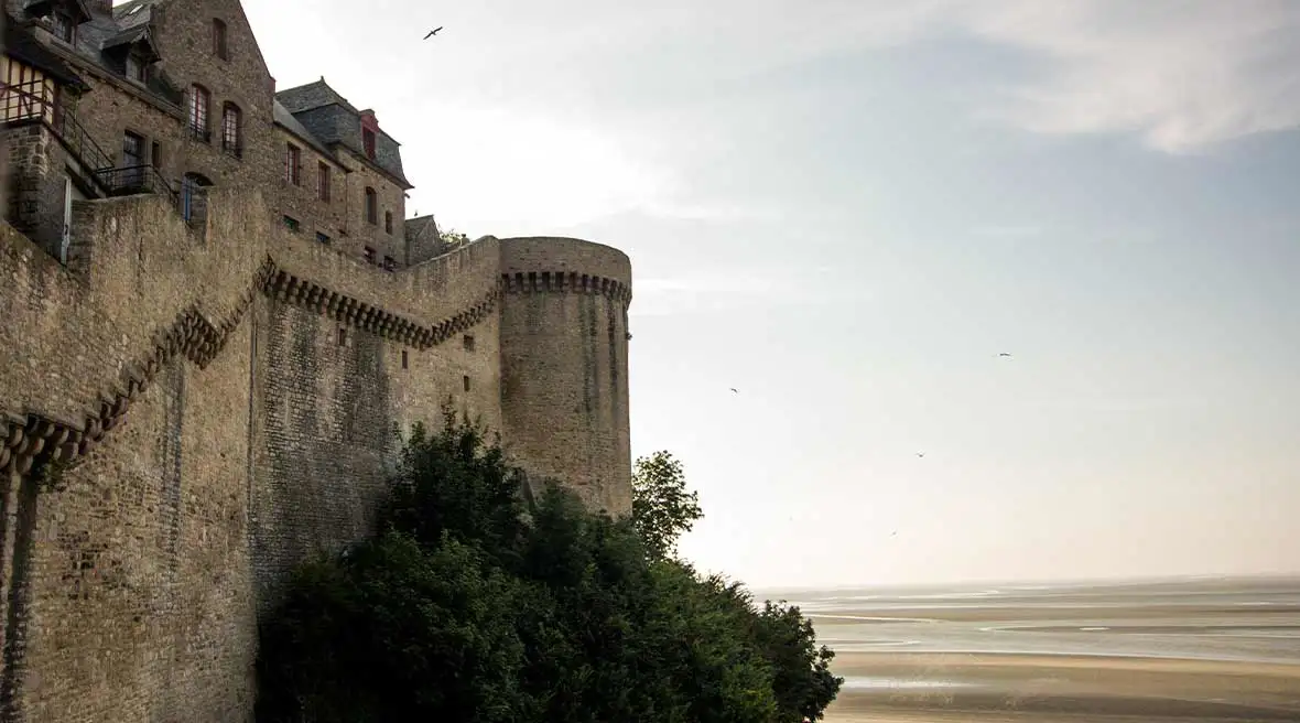 Steps and fortifications on the left hand side of the picture with a green tree to the right and yellow sands with the sunset in the back ground