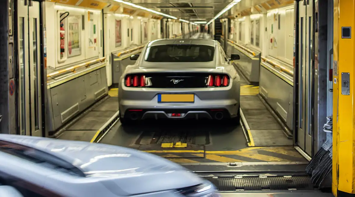 Cars driving onto a train carriage silver sports car already inside and a blue car following